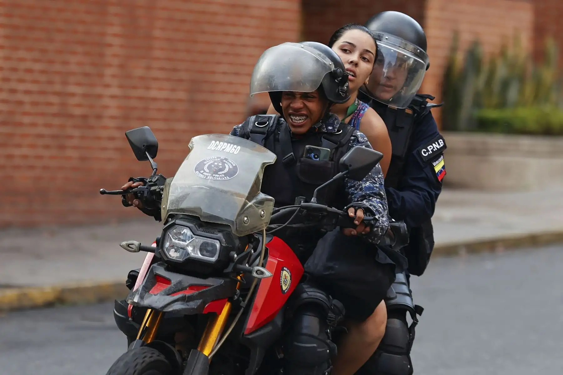 Miembros del Cuerpo de Policía Nacional Bolivariana (CPNB) llevan a una mujer en una motocicleta durante enfrentamientos por los resultados de las elecciones presidenciales este lunes, en Caracas (Venezuela). 
Foto: EFE