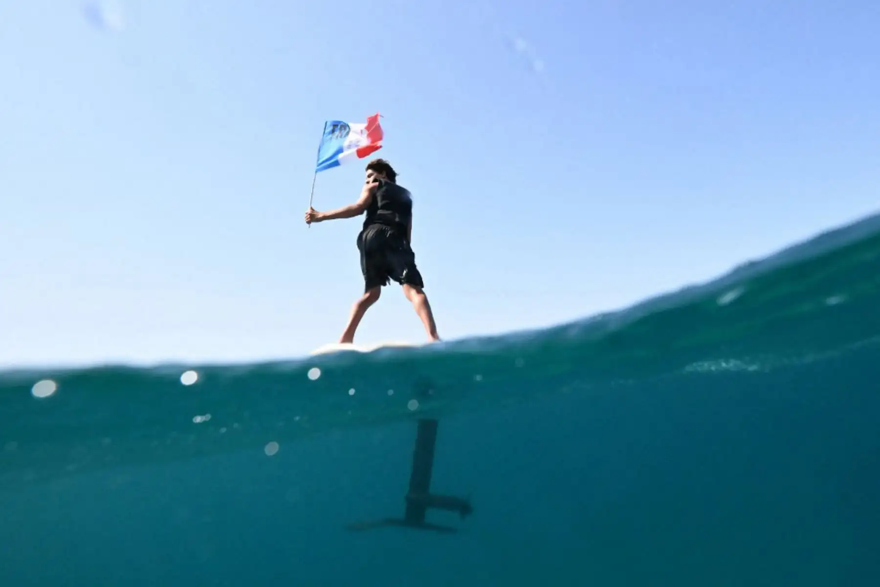 Un partidario de Francia en un florete sostiene banderas nacionales en el mar antes del inicio de las competiciones de vela durante los Juegos Olímpicos de París 2024 en el puerto deportivo Roucas-Blanc de Marsella. Foto: AFP