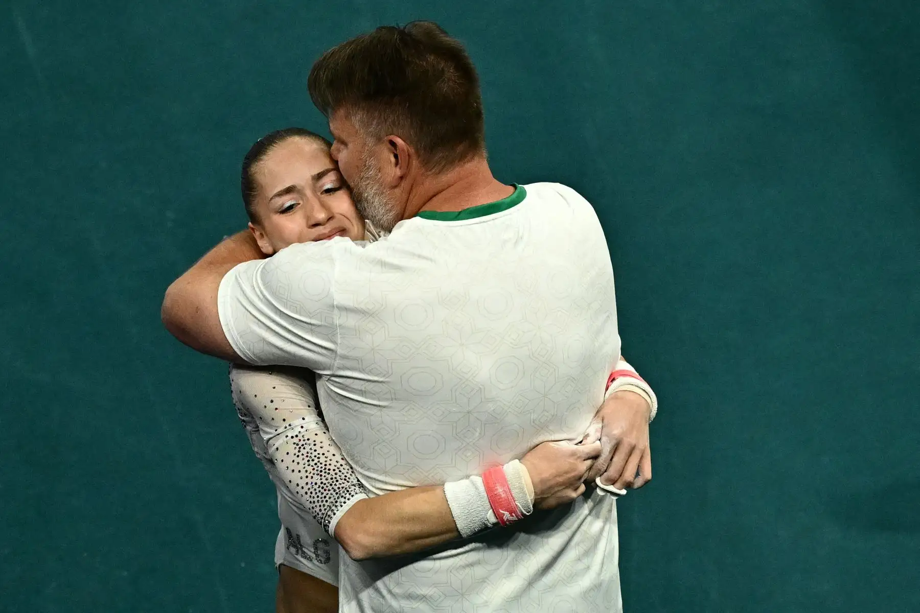 La argelina Kaylia Nemour es felicitada por su entrenador tras competir en la final de barras asimétricas femeninas de gimnasia artística durante los Juegos Olímpicos París 2024. AFP