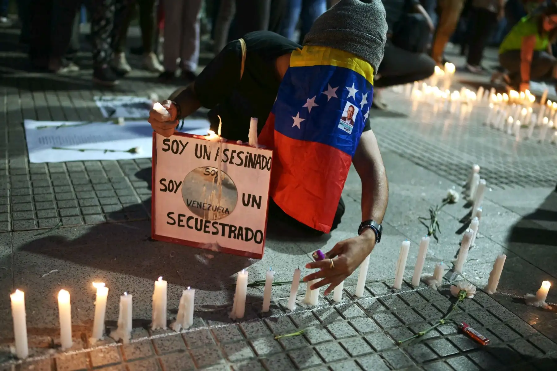Una mujer cubierta con una bandera venezolana enciende velas durante una vigilia convocada por la oposición política en Caracas, Venezuela, exigiendo la libertad de los presos políticos arrestados durante las protestas tras la impugnada reelección del presidente Nicolás Maduro. Foto: AFP