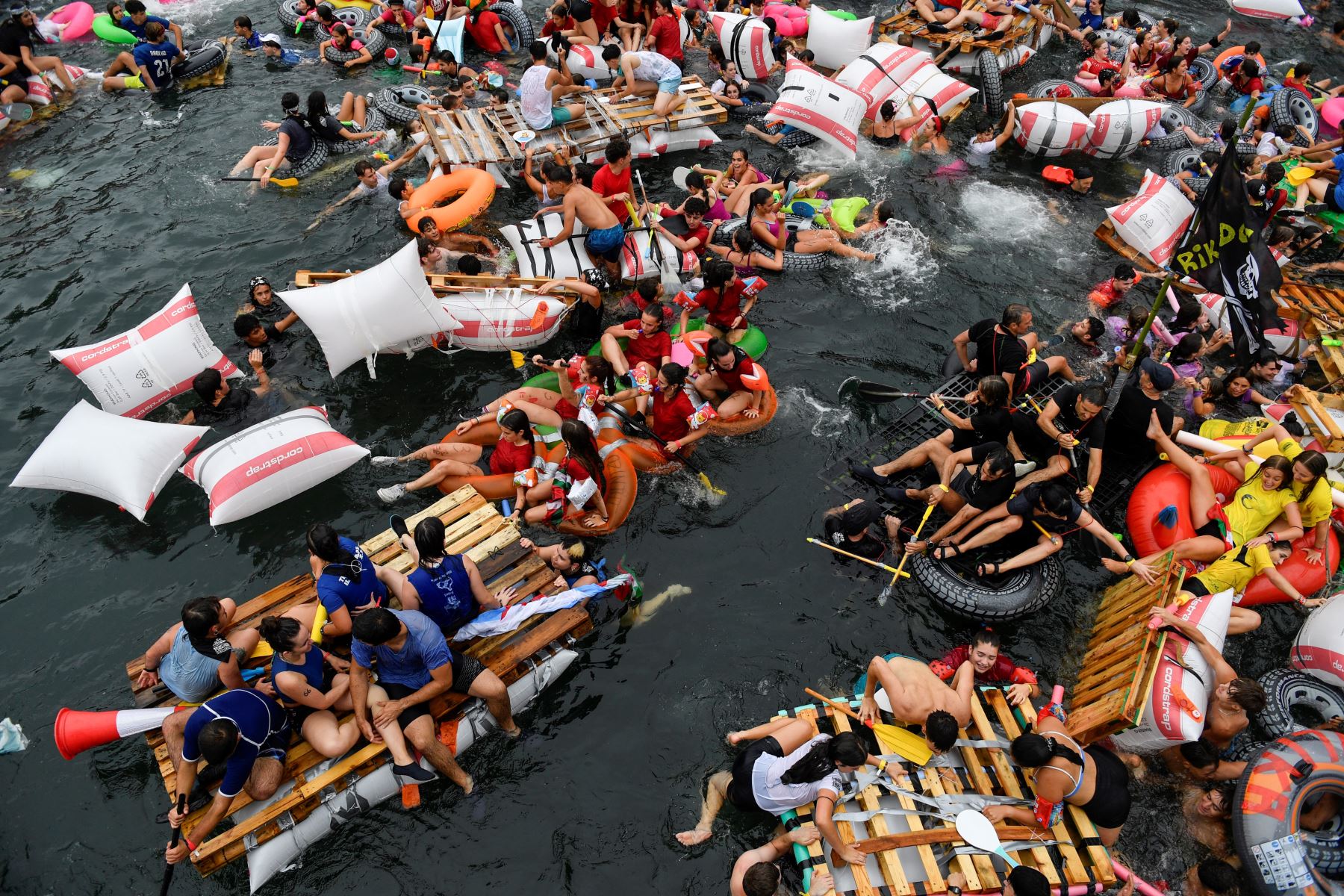 Jóvenes españoles abandonan el puerto en balsas improvisadas antes de llegar a la bahía de La Concha durante el Festival "Pirata Abordaia" en la ciudad vasca de San Sebastián, en España, el 12 de agosto de 2024. Foto: AFP