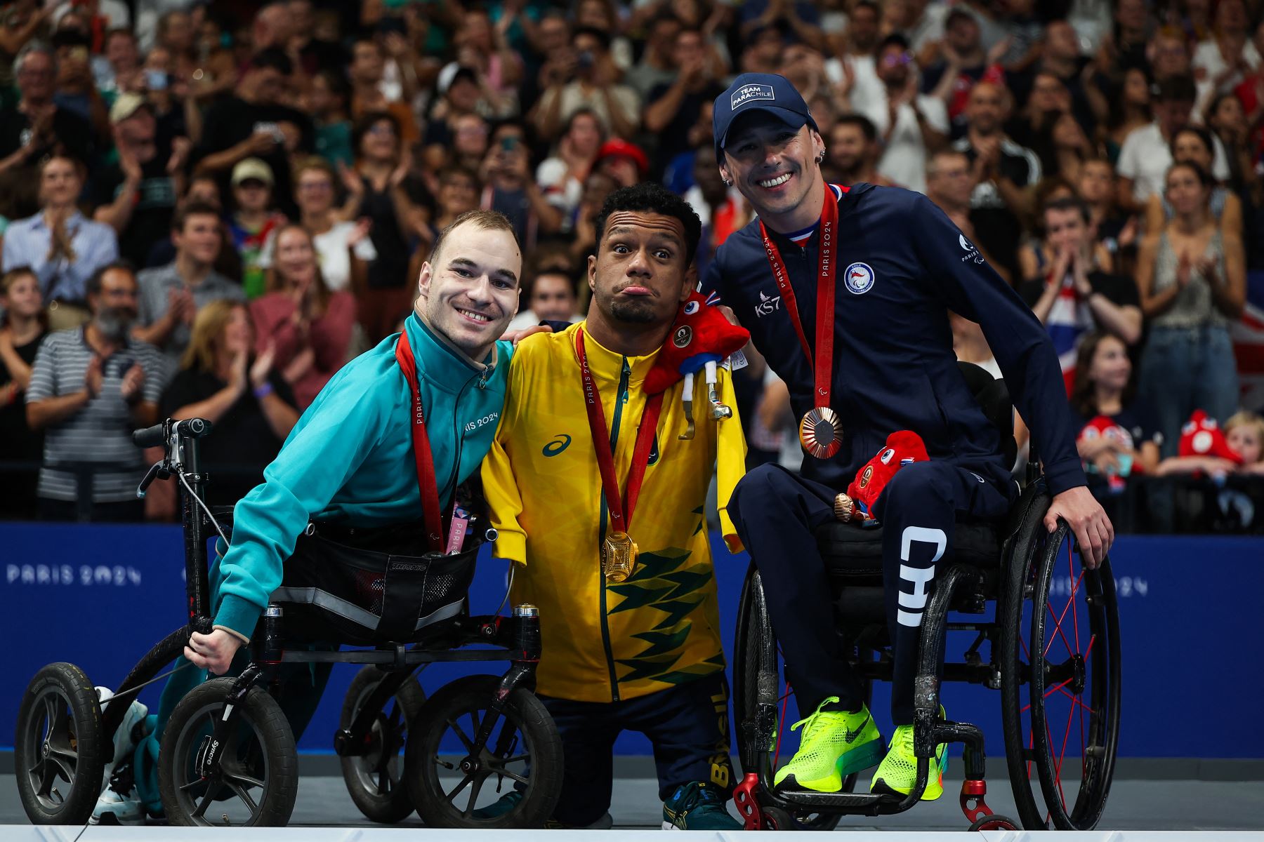 Los atletas paralímpicos neutrales Vladimir Danilenko, medallista de plata, Gabriel Geraldo dos Santos Araujo, medallista de oro de Brasil, y Alberto Caroly Abarza Diaz, medallista de bronce de Chile, celebran en el podio del evento masculino de natación espalda S2 100m durante los Juegos Paralímpicos París 2024 en París La Defense Arena en Nanterre, en Francia. Foto: AFP