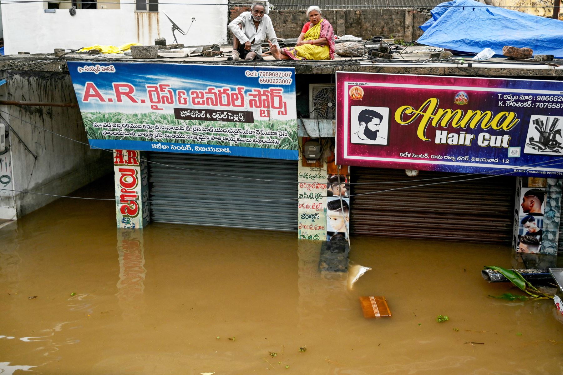 La gente se sienta en el techo de las tiendas mientras se refugia en medio de las inundaciones tras las fuertes lluvias monzónicas, en Vijayawada.
Foto: AFP