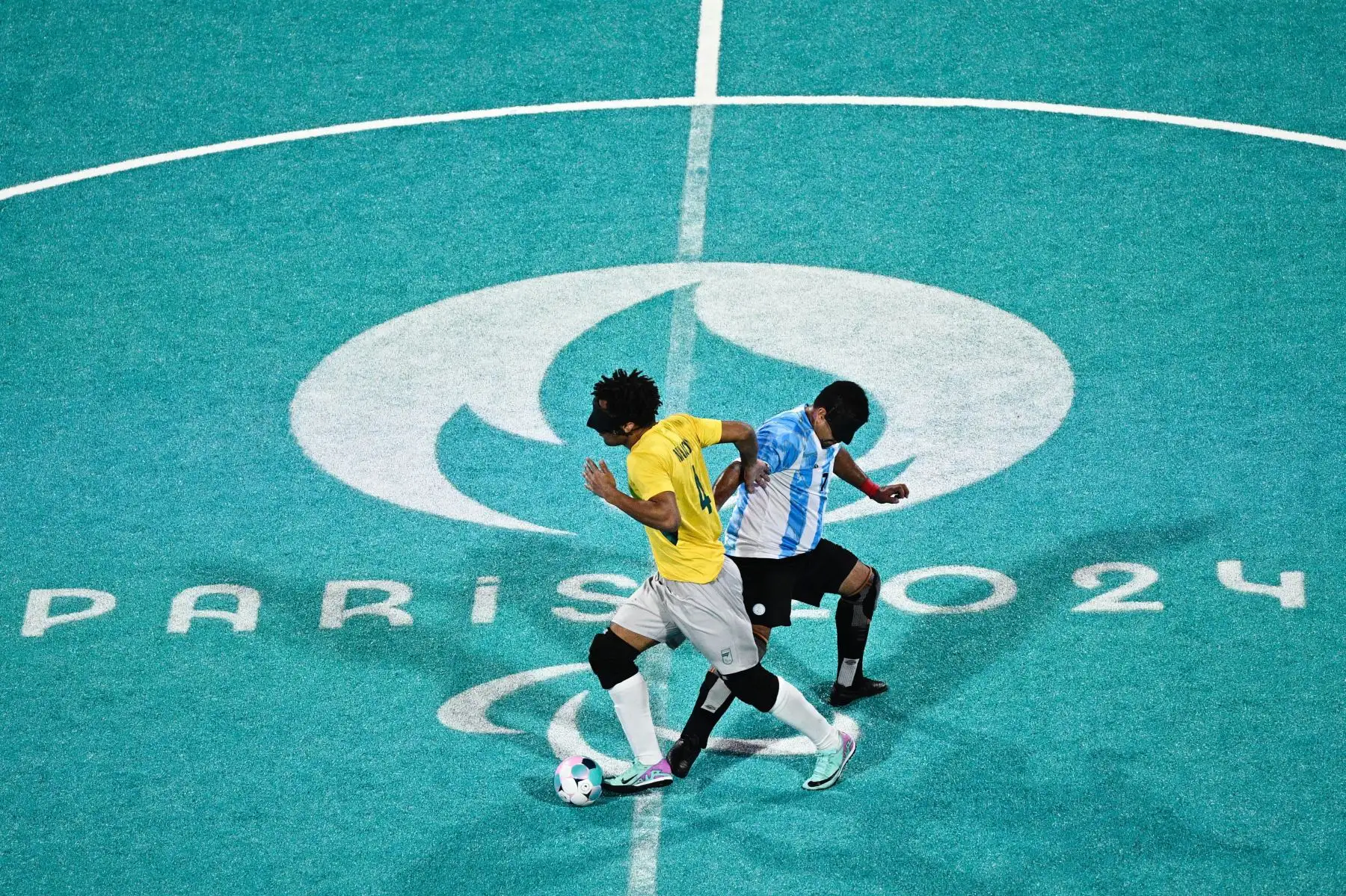 El brasileño Maicon Junior dos Santos Mendes  lucha por el balón con el argentino Maximiliano Espinillo durante el partido de semifinales de fútbol para ciegos masculino entre Brasil y Argentina de los Juegos Paralímpicos de París 2024. 
Foto: ANDINA/AFP