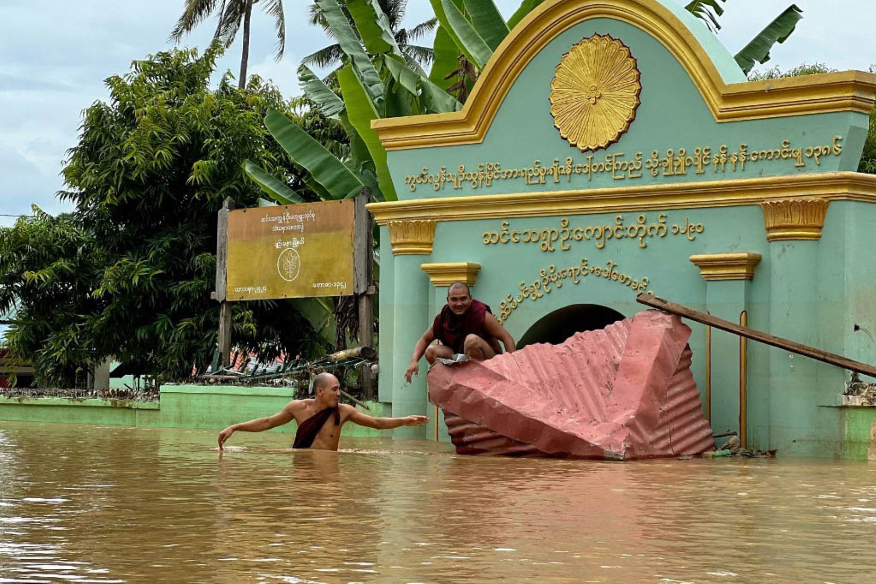 Un monje budista camina a través de las aguas de la inundación mientras otro se sienta en un techo roto frente a un monasterio en la aldea de Sin Thay en Pyinmana, en la región de Naypyidaw en Myanmar. Foto: AFP