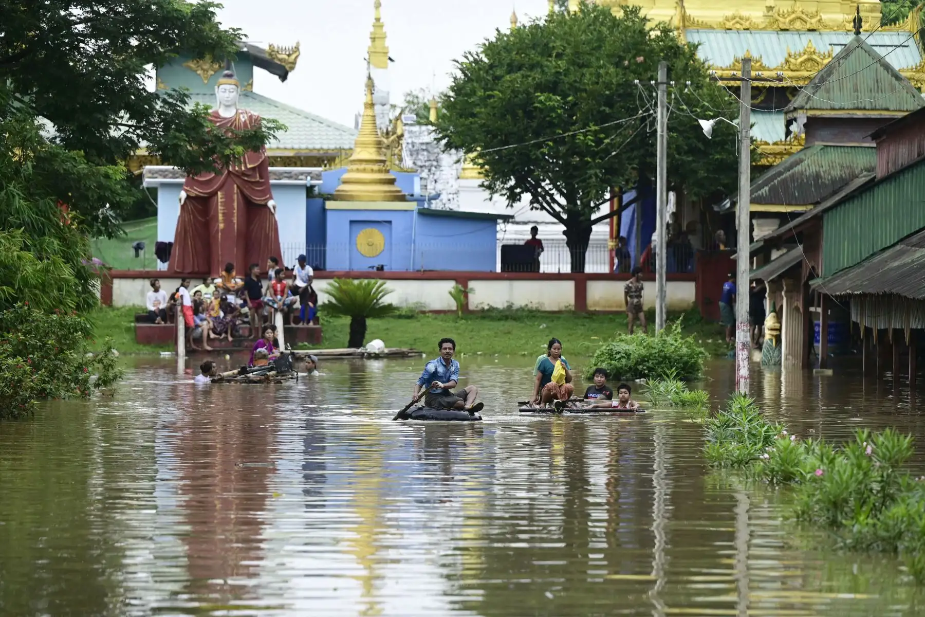 Los residentes afectados por las inundaciones se suben a balsas de bambú mientras otros se reúnen en terrenos más altos junto a un templo en Taungoo, región de Bago, Myanmar, el 14 de septiembre de 2024, tras las fuertes lluvias que siguieron al paso del tifón Yagi. El tifón Yagi provocó un colosal diluvio de lluvia que inundó una franja del norte de Vietnam. Foto: ANDINA/AFP
