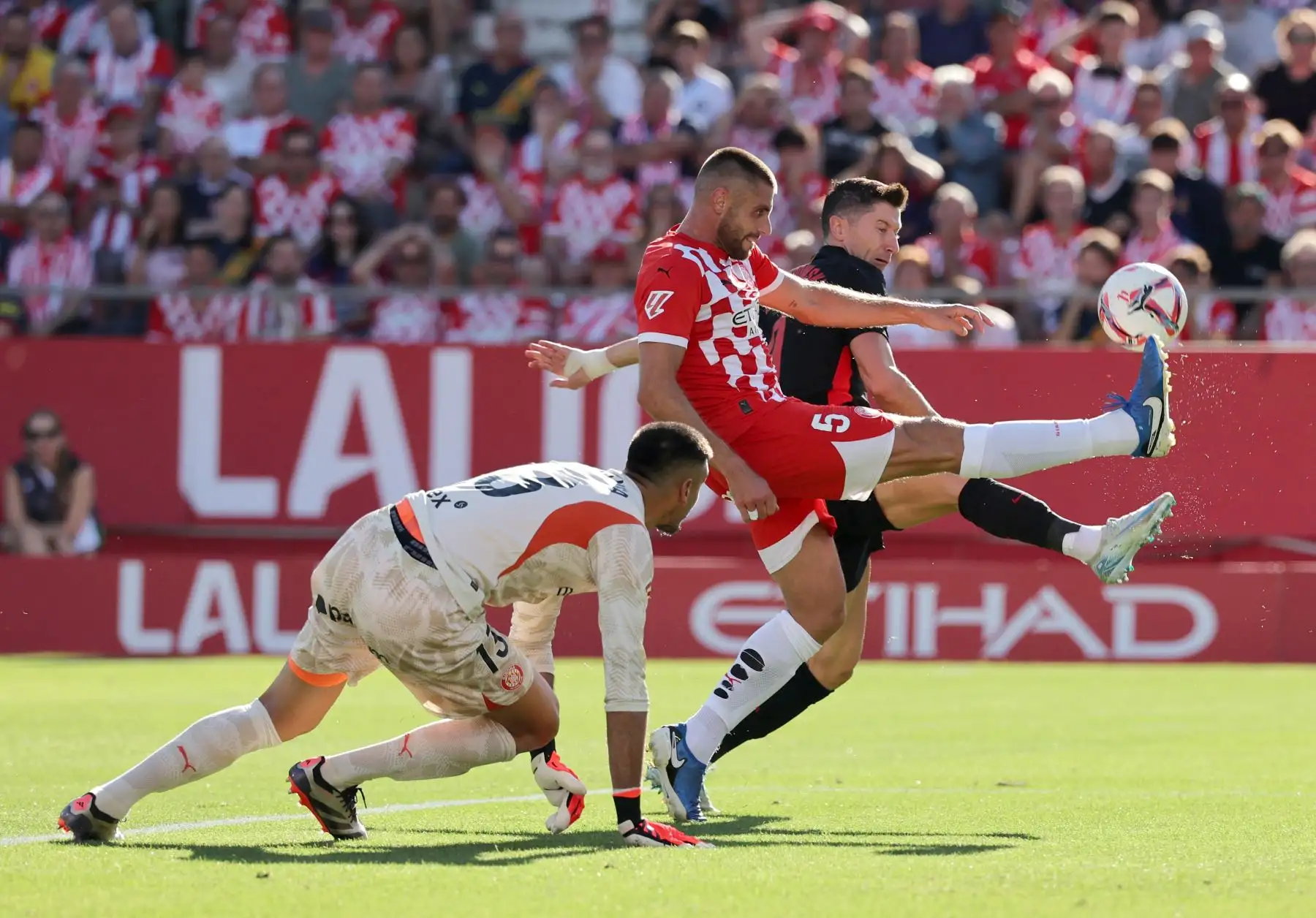 El delantero polaco del Barcelona, ​​Robert Lewandowski, lucha por el balón con el defensa español del Girona, David López, y el portero argentino del Girona, Paulo Gazzaniga, durante el partido de fútbol de la liga española entre el Girona FC y el FC Barcelona. Foto: ANDINA/ AFP