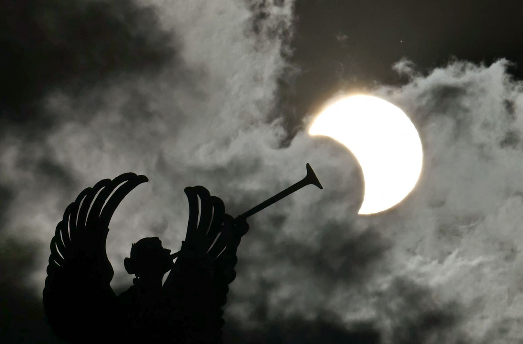 Vista parcial del eclipse anular solar se muestra detrás de un monumento a los Ángeles en el edificio del Congreso Nacional en Buenos Aires. AFP