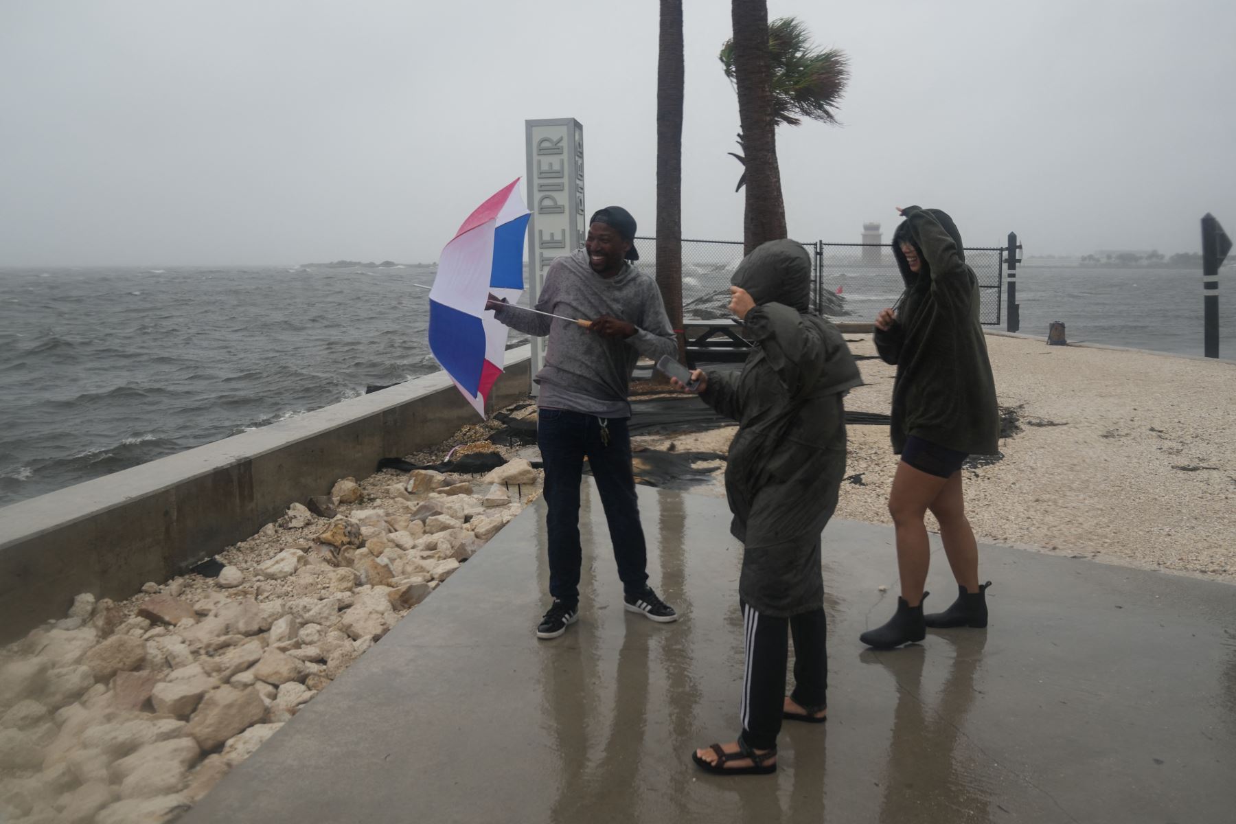 Jeremy Beal, Micaela Robertson y Alex Quintos reaccionan cuando las olas rompen a lo largo del muelle de St. Pete en San Petersburgo, Florida, mientras se espera que el huracán Milton toque tierra esta noche. AFP