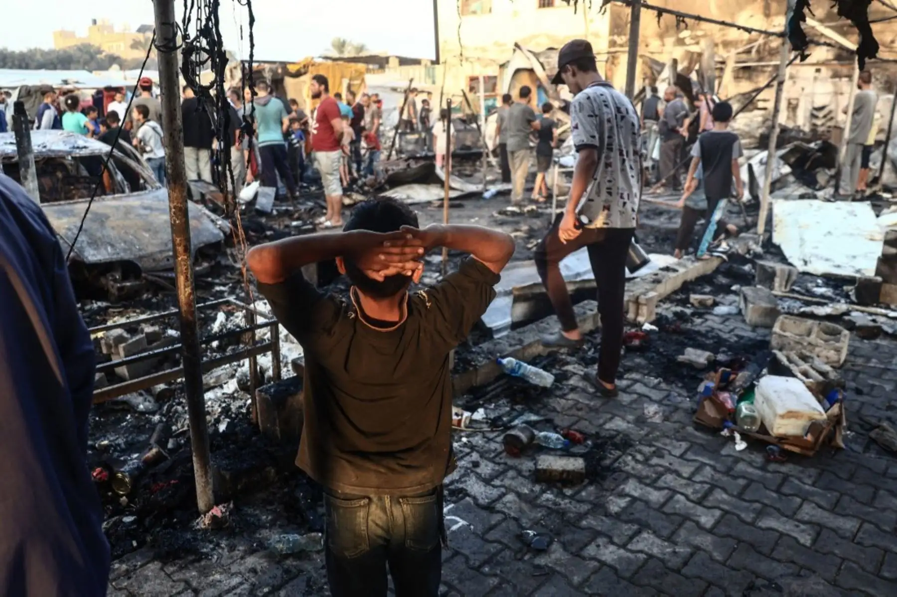 Un niño palestino hace gestos mientras la gente camina en medio de la destrucción tras un ataque del ejército israelí alrededor de tiendas de campaña para personas refugiadas dentro de los muros del Hospital de los Mártires de Al-Aqsa en Deir al-Balah, en el centro de la Franja de Gaza. Foto:  AFP
