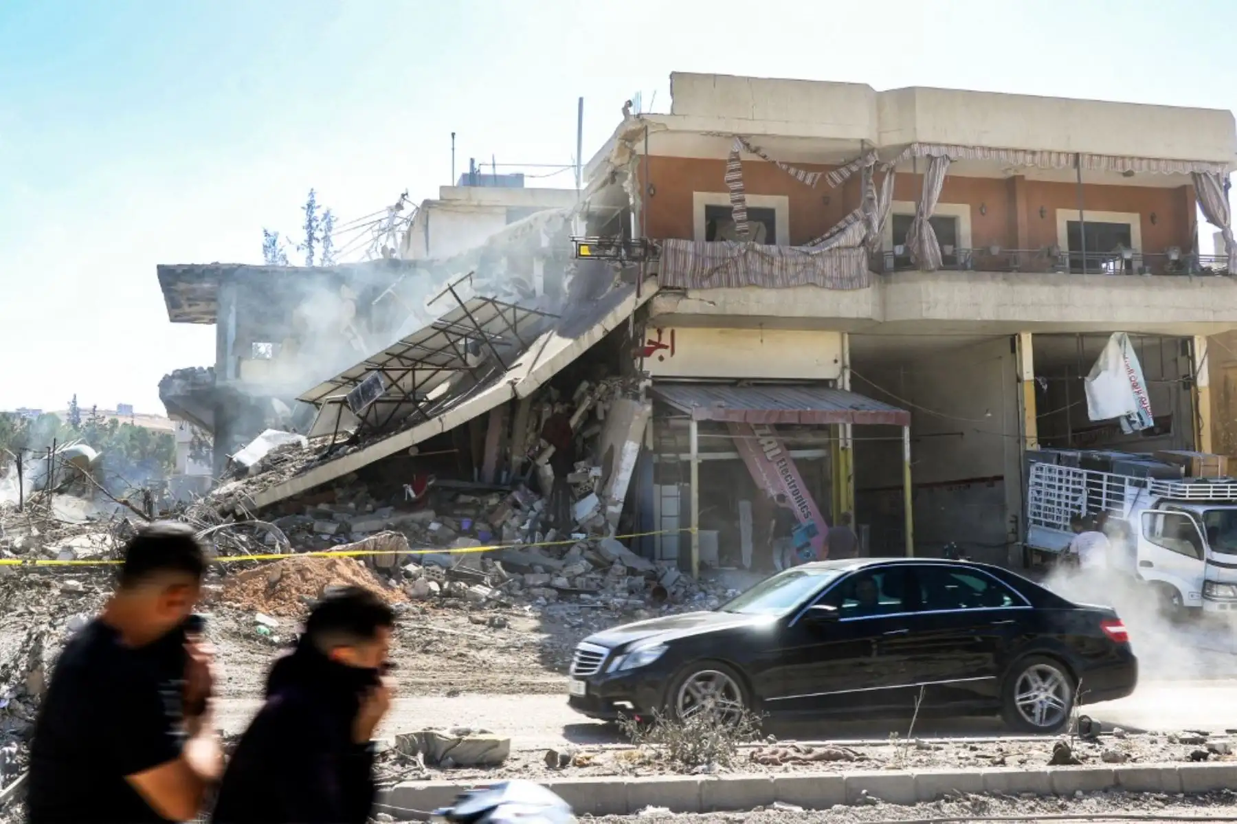 Hombres se cubren la cara mientras un vehículo deja rastros de polvo al pasar por un edificio destruido tras un ataque aéreo israelí en la aldea de Douris, al sureste de Baalbek, en el valle de Bekaa oriental del Líbano. Foto: AFP