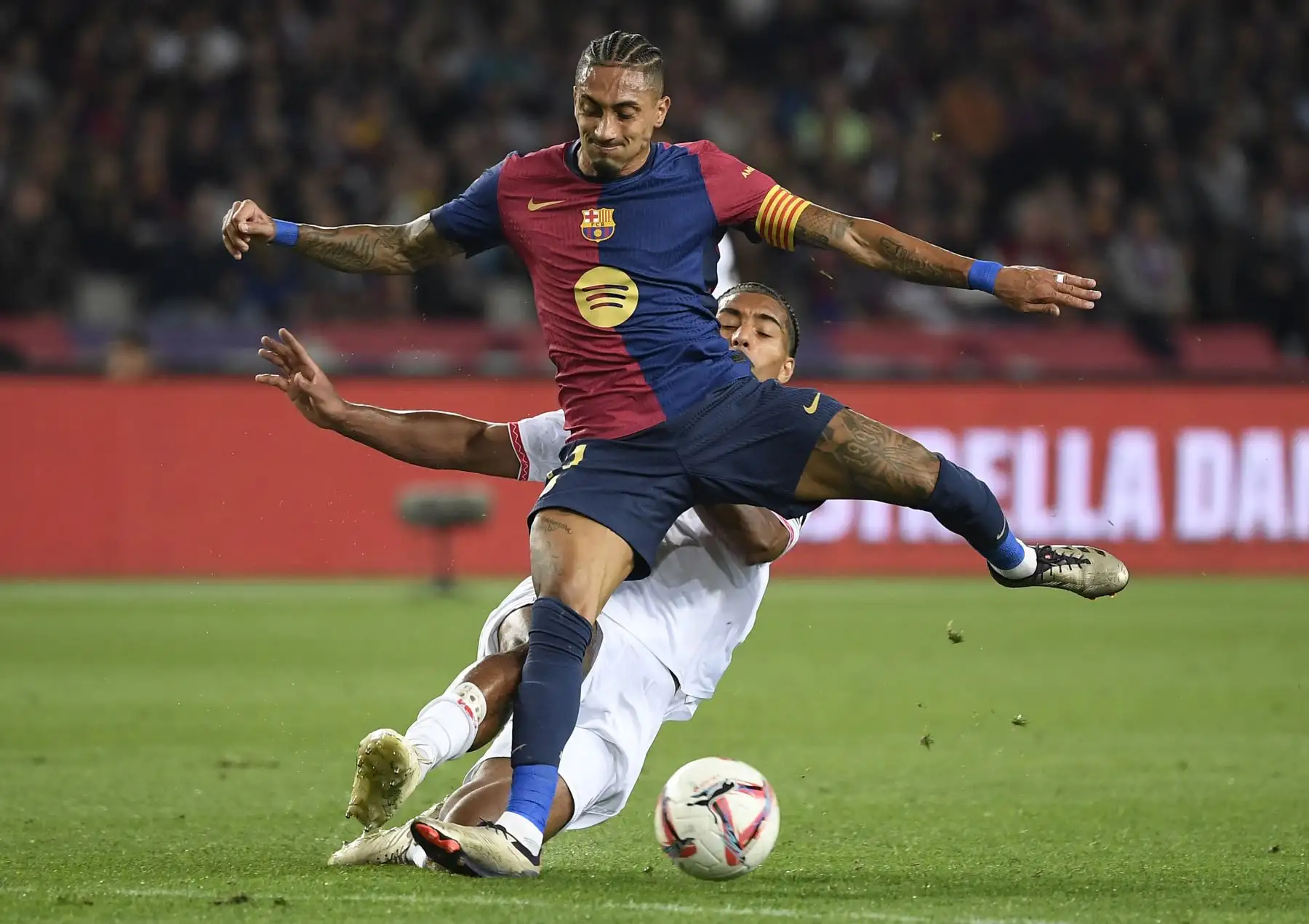 El defensa francés del Sevilla, Loic Bade, y el delantero brasileño del Barcelona, ​​Raphinha, compiten por el balón durante el partido de fútbol de la liga española entre el FC Barcelona y el Sevilla FC en el Estadi Olimpic Lluis Companys en Barcelona. Foto: ANDINA/ AFP
