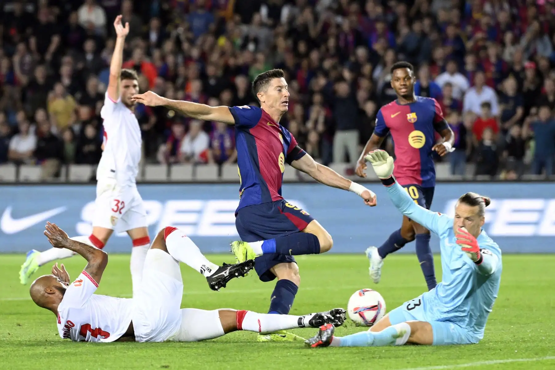 El defensa brasileño del Sevilla, Marcao Teixeira, el delantero polaco del Barcelona, ​​Robert Lewandowski, y el portero noruego del Sevilla, Orjan Haskjold Nyland, compiten por el balón durante el partido de fútbol de la liga española entre el FC Barcelona y el Sevilla FC en el Estadi Olimpic Lluis Companys en Barcelona. Foto. ANDINA/ AFP