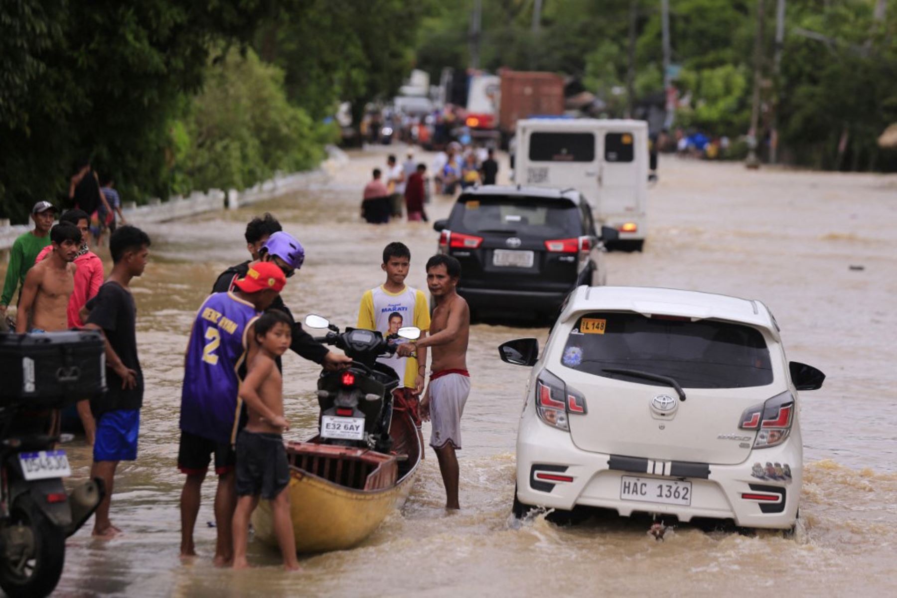 La gente carga una motocicleta en un bote de madera mientras los vehículos maniobran a través de una carretera inundada a causa de las fuertes lluvias provocadas por la tormenta tropical Trami, en la ciudad de Nabua, provincia de Camarines Sur de Manila. Foto AFP