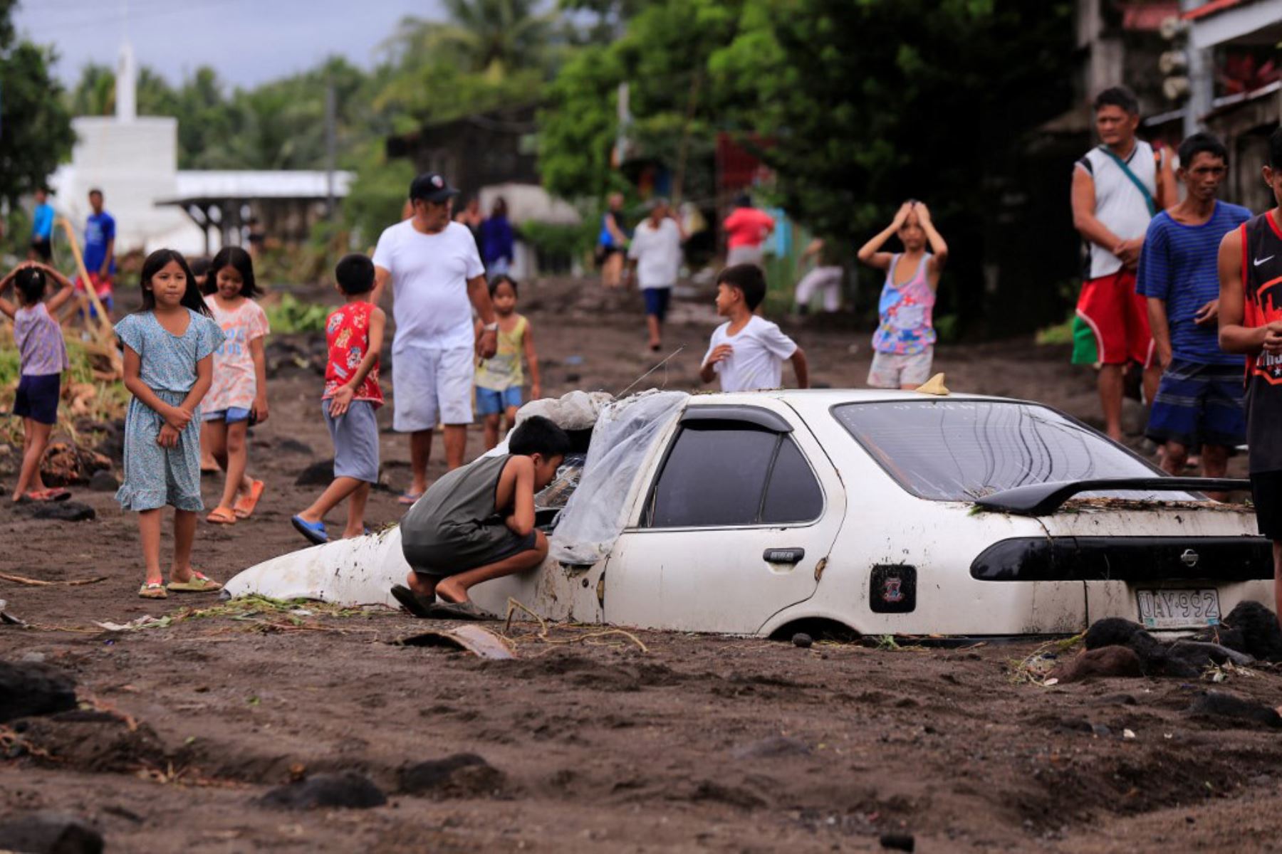 Los residentes observan un automóvil enterrado por las cenizas volcánicas que cayeron en cascada sobre un pueblo debido a las fuertes lluvias provocadas por la tormenta tropical Trami en un pueblo de la ciudad de Guinobatan, provincia de Albay, al sur de Manila.Foto AFP