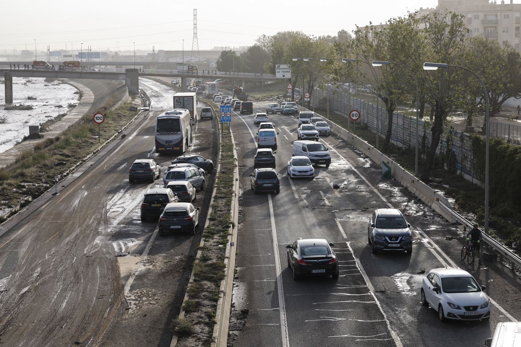 Varios coches circulan entre los vehículos afectados por la dana en la V30 a la altura de La Torre este viernes en Valencia. Los servicios de emergencia siguen trabajando en tareas de desescombro tras la devastadora dana que ha dejado al menos 95 fallecidos y que continuará en algunas zonas. Foto: EFE