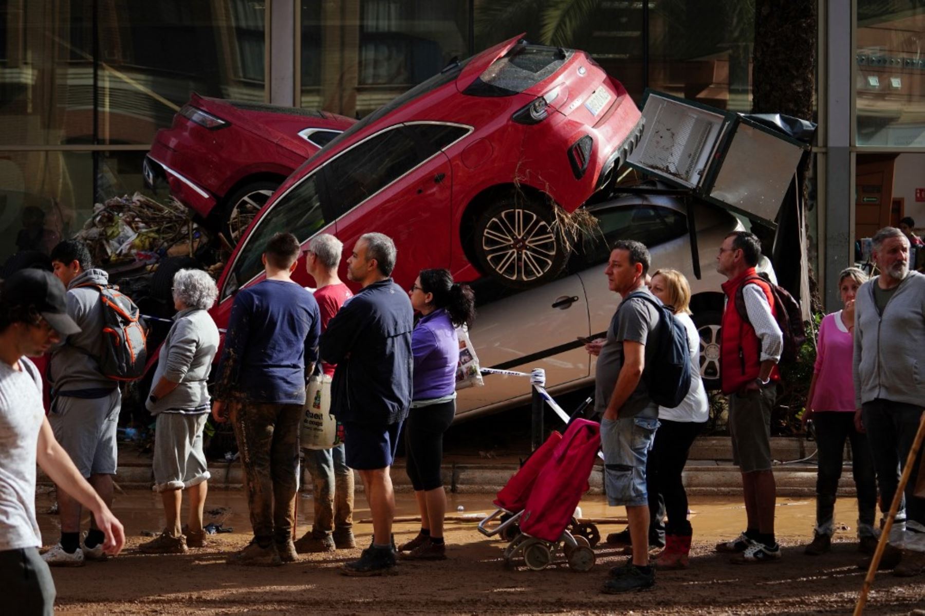 Personas hacen cola para recibir suministros cerca de una pila de coches destrozados el 1 de noviembre de 2024, tras los devastadores efectos de las inundaciones en la ciudad de Paiporta, en la región de Valencia, al este de España. Foto: AFP