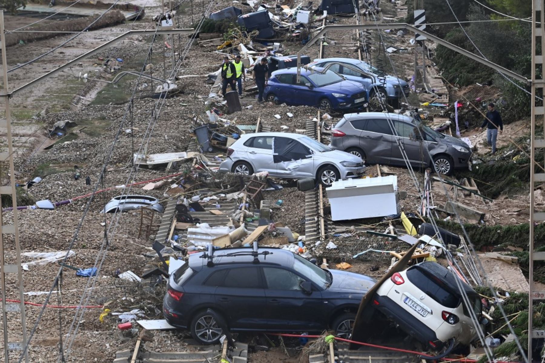 Esta fotografía tomada el 1 de noviembre de 2024 muestra a personas caminando entre autos destrozados esparcidos a lo largo de la vía férrea después de la devastadora inundación en la ciudad de Alfafar, en la región de Valencia, al este de España. Foto: AFP