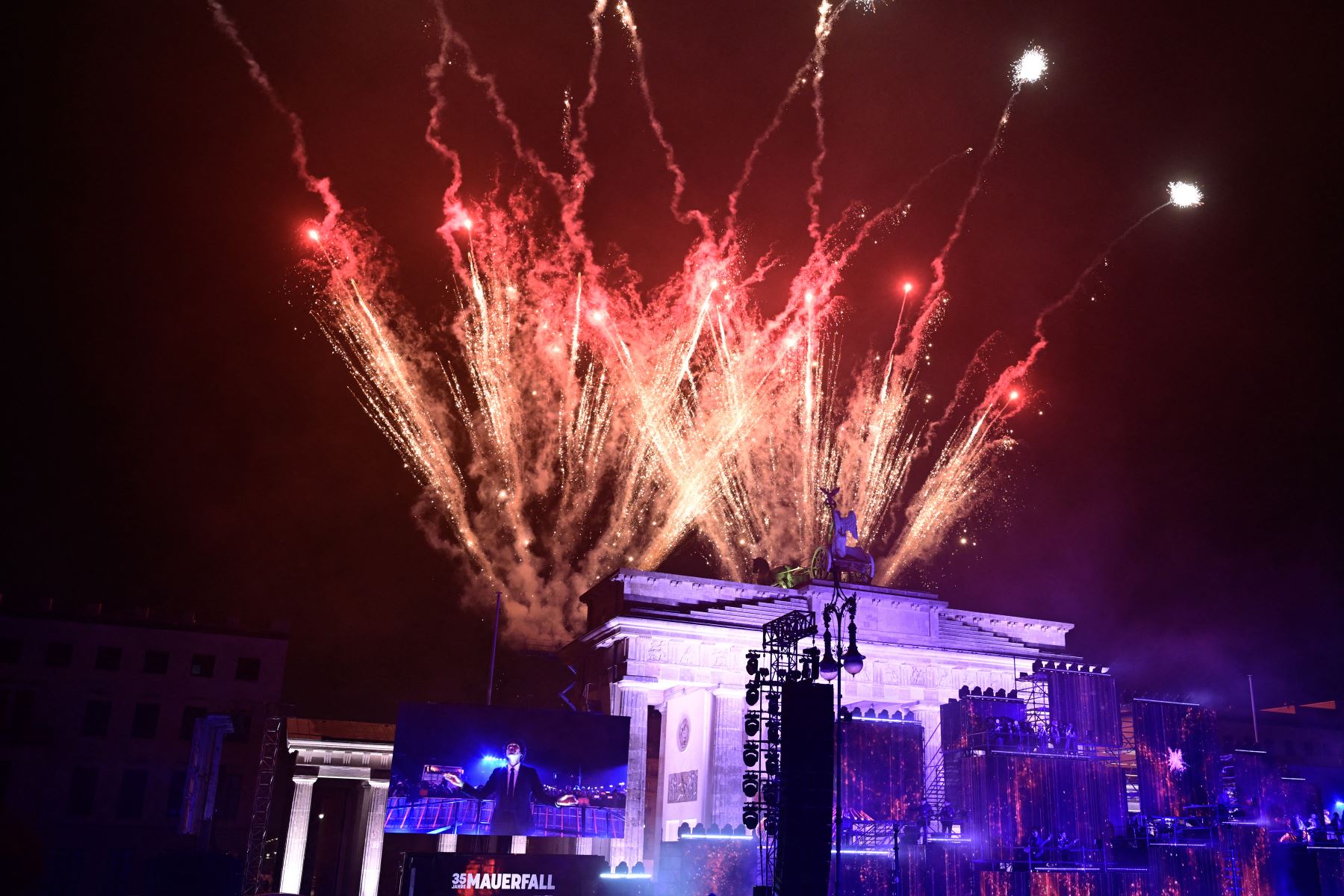 Los fuegos artificiales iluminan el cielo sobre la Puerta de Brandeburgo mientras los músicos tocan en el escenario durante el "Konzert für Freiheit"con motivo del 35º aniversario de la caída del Muro de Berlín.
Foto: AFP