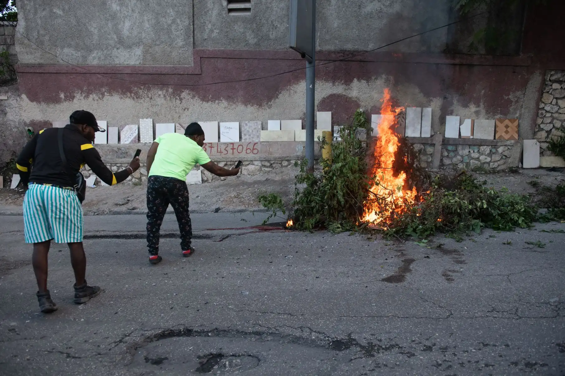 Personas toman fotos con sus teléfonos a una hoguera , en una calle de Puerto Príncipe (Haití). Al menos 28 presuntos miembros de grupos armados fueron abatidos en la zona metropolitana de Puerto Príncipe por miembros de la Policía Nacional.
Foto: EFE