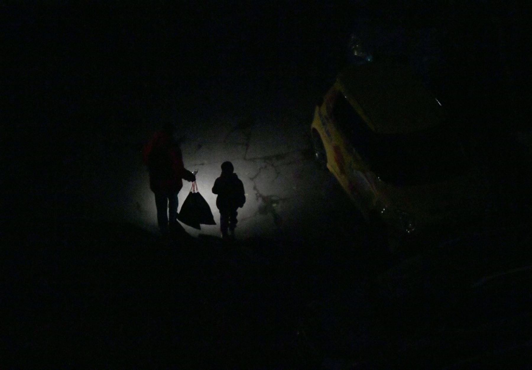 Un hombre enciende una linterna mientras camina junto a su hijo por una calle oscura durante un apagón en Kiev el 19 de noviembre de 2024, provocado por un bombardeo aéreo masivo en medio de la invasión rusa en Ucrania. Foto: AFP