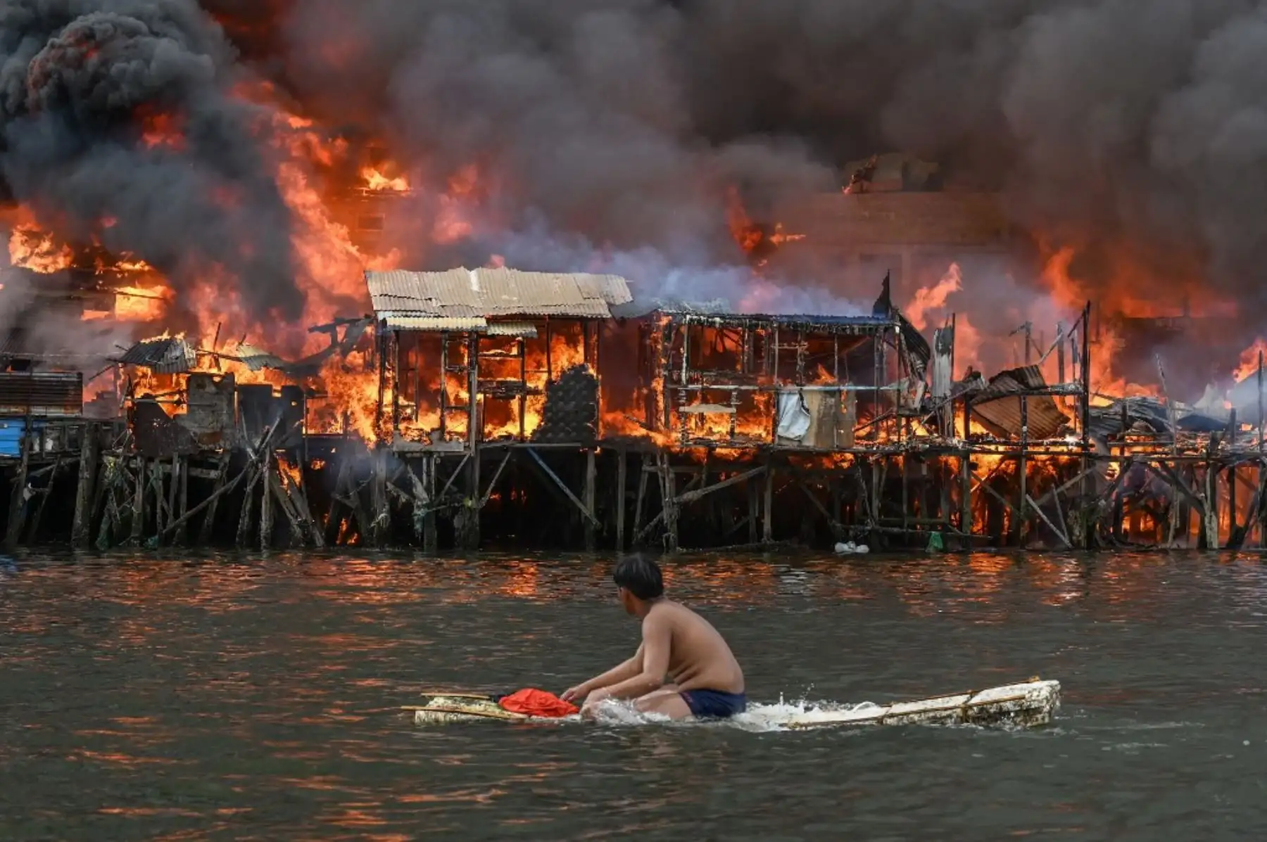 Un hombre observa casas en llamas en Tondo en Manila el 24 de noviembre de 2024. Llamas naranjas enfurecidas y humo negro espeso se escalaban hacia el cielo, mientras el fuego atravesaba cientos de casas en un barrio pobre construido de la capital filipina Manila. (Foto de JAM STA ROSA / AFP)