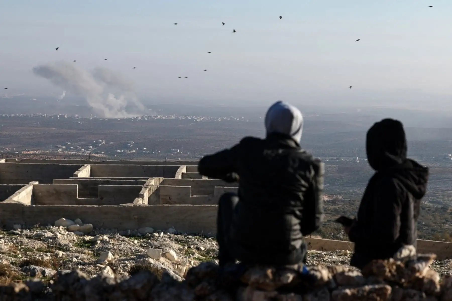 En esta imagen tomada desde el pueblo de Ariha, en el norte de Siria, la gente observa cómo el humo se eleva desde el lugar de los enfrentamientos y el bombardeo mutuo entre los yihadistas sirios y las facciones aliadas y las fuerzas del régimen en las líneas del frente en las afueras de la ciudad de Saraqib en la provincia siria de Alepo el 28 de noviembre de 2024. Un monitor de la guerra de Siria dijo el 28 de noviembre que los enfrentamientos entre el ejército y los yihadistas mataron a más de 130 combat