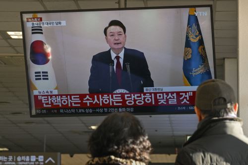 La gente mira una pantalla que muestra al presidente de Corea del Sur, Yoon Suk Yeol, pronunciando un discurso televisado en una terminal de autobuses en Seúl. Foto: ANDINA/AFP