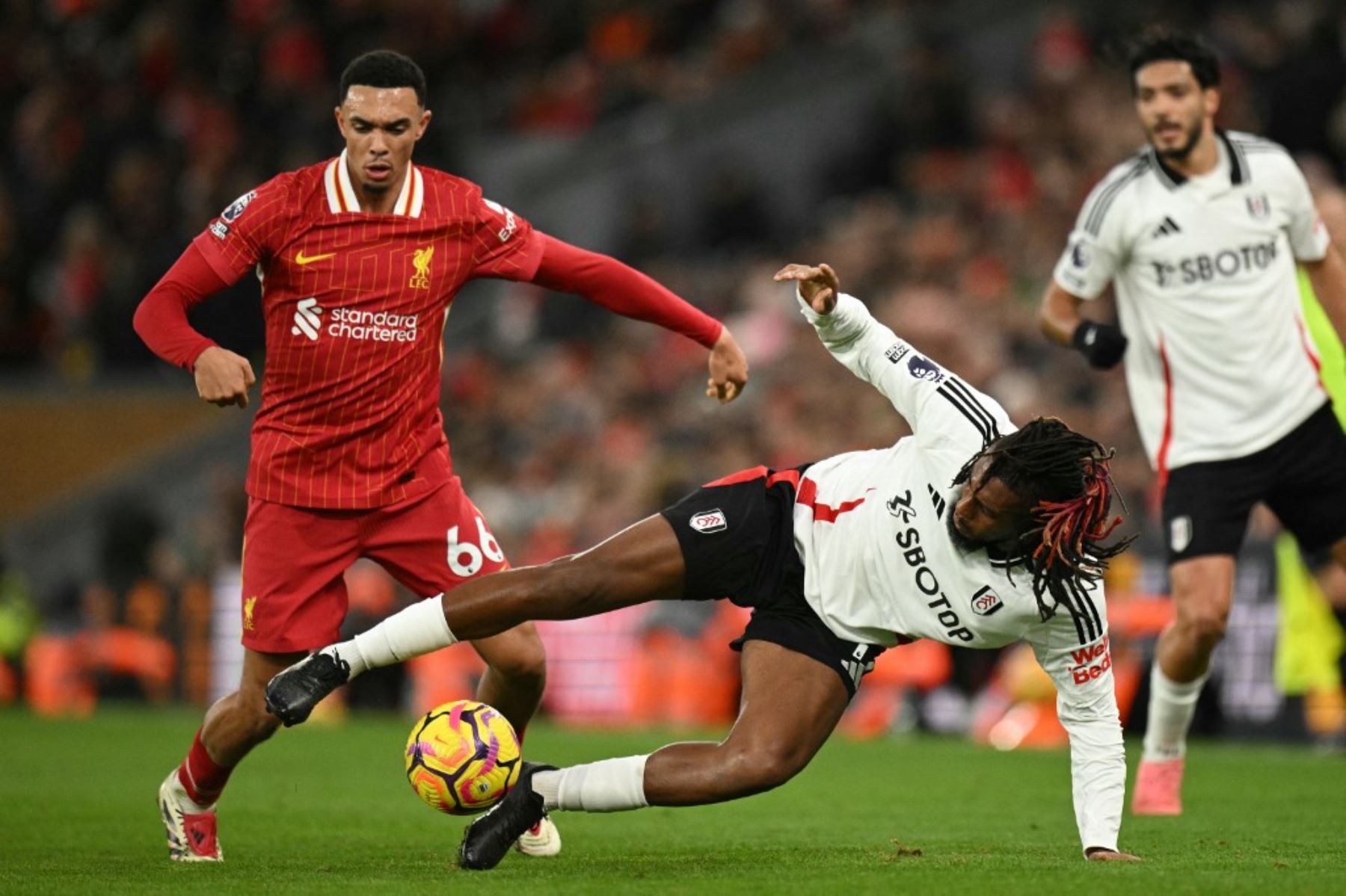 El defensor inglés del Liverpool #66 Trent Alexander-Arnold (L) compite con el centrocampista nigeriano del Fulham #17 Alex Iwobi (C) durante el partido de fútbol de la Premier League inglesa entre Liverpool y Fulham en Anfield en Liverpool, noroeste de Inglaterra, el 14 de diciembre de 2024. (Foto de Oli SCARFF / AFP)