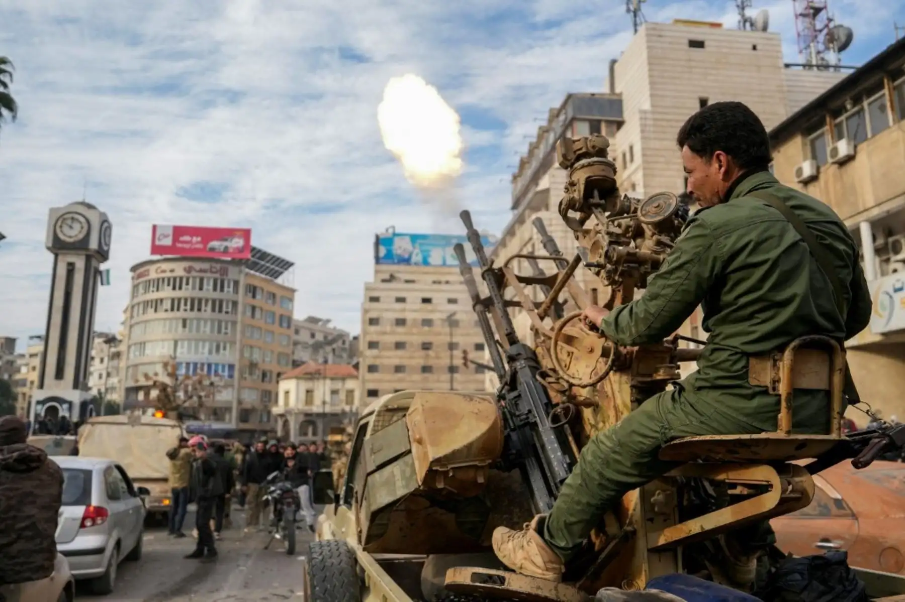 Un combatiente rebelde sirio dispara rondas mientras la gente celebra cerca de la Torre del Reloj en la ciudad central de Homs el 8 de diciembre de 2024, después de que las fuerzas rebeldes entraran en la tercera ciudad de Siria durante la noche. Los rebeldes liderados por islamistas declararon que habían tomado Damasco en una ofensiva relámpago el 8 de diciembre, enviando al presidente Bashar al-Assad huyendo y poniendo fin a cinco décadas de gobierno de Baath en Siria. (Foto de MUHAMMAD HAJ KADOUR / AFP)