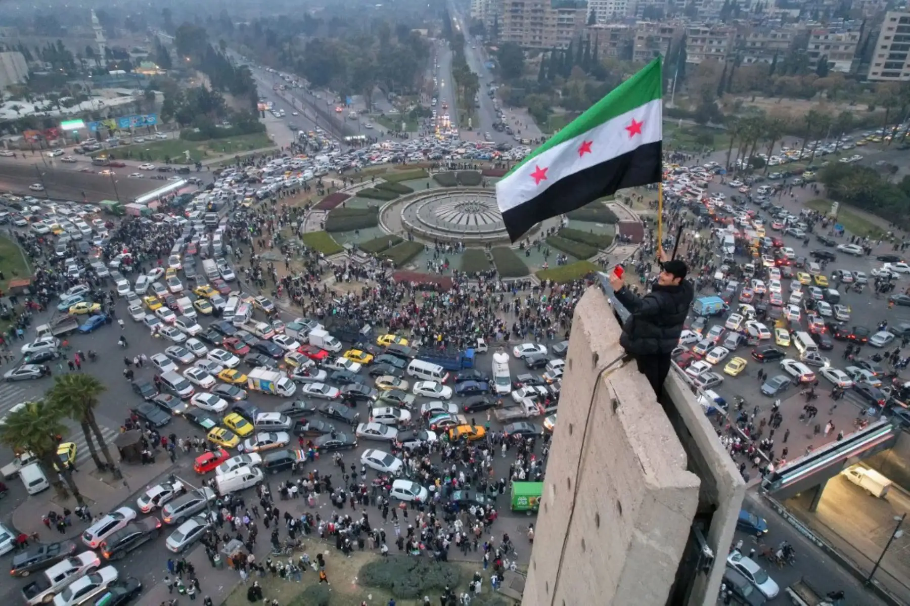 Una vista aérea muestra a un hombre sirio ondeando la bandera siria de la era de la independencia en la plaza omeya central de Damasco el 11 de diciembre de 2024. (Foto de Bakr ALKASEM / AFP)