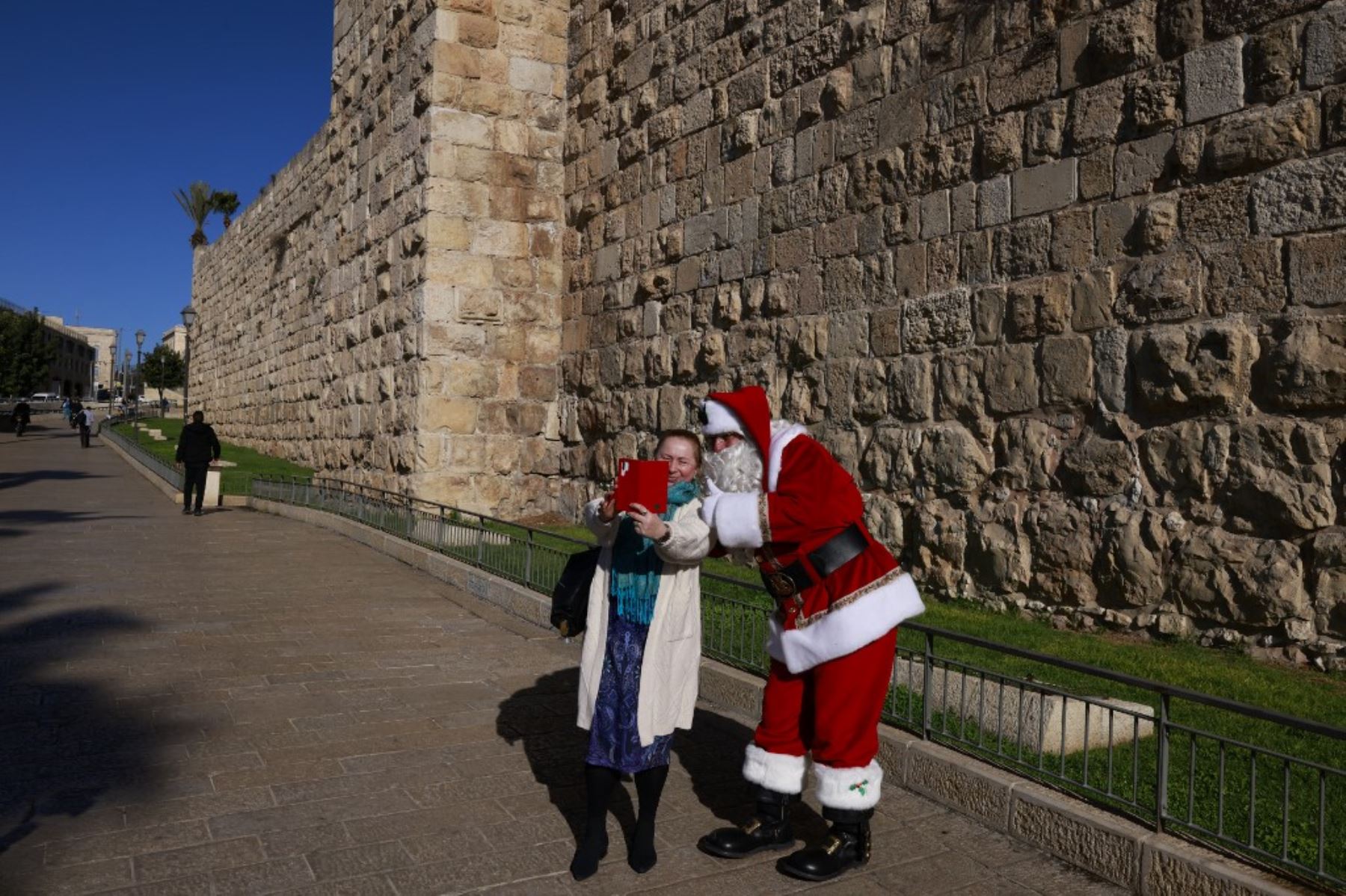 El palestino Issa Kassissieh, vestido de Papá Noel, posa para una selfie con un transeúnte en la Puerta de Jaffa en la Ciudad Vieja de Jerusalén el 19 de diciembre de 2024, antes de las celebraciones por Navidad. Foto: AFP