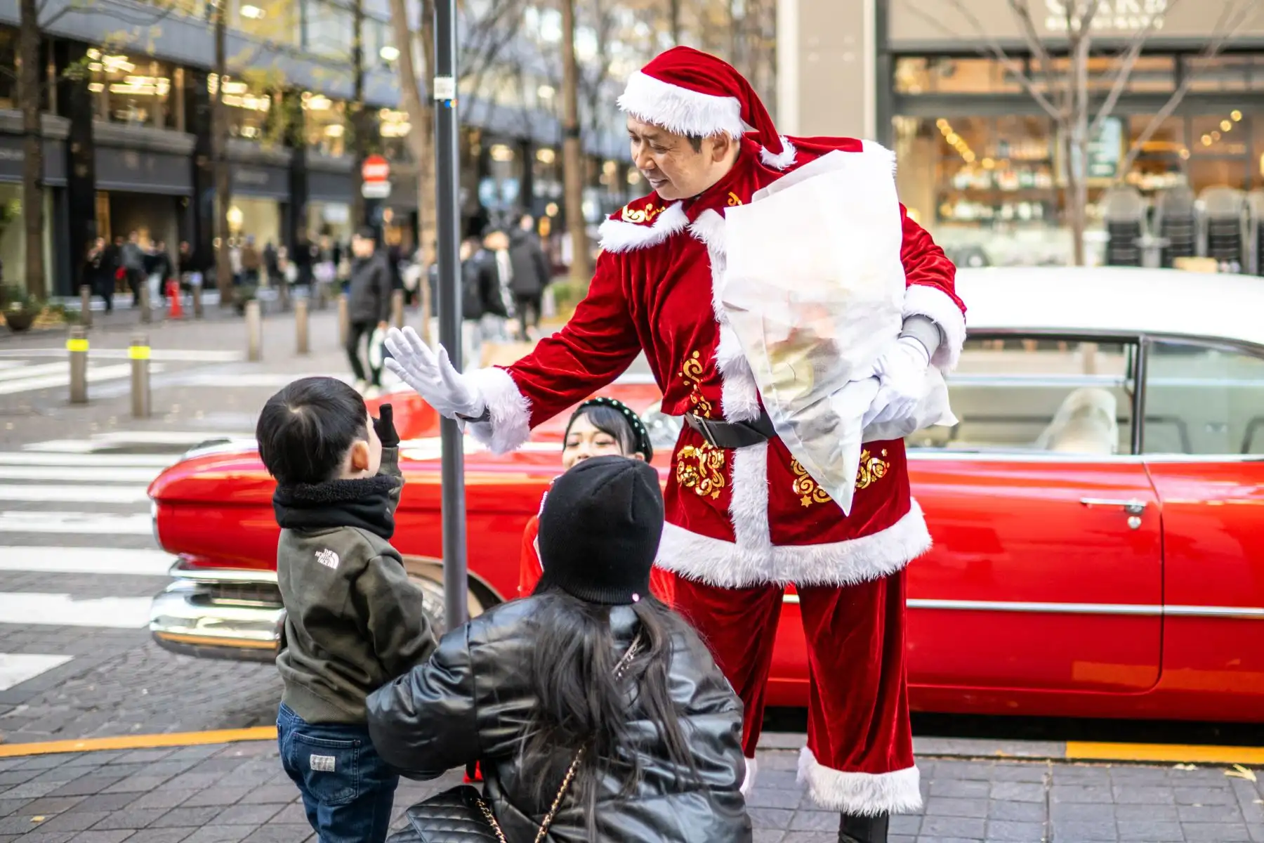 Hiroyuki Wada (derecha), miembro de un grupo de coches clásicos, vestido como Papá Noel, da regalos de Navidad a los niños en una calle de la zona de Marunouchi de Tokio, Japón. Foto: AFP