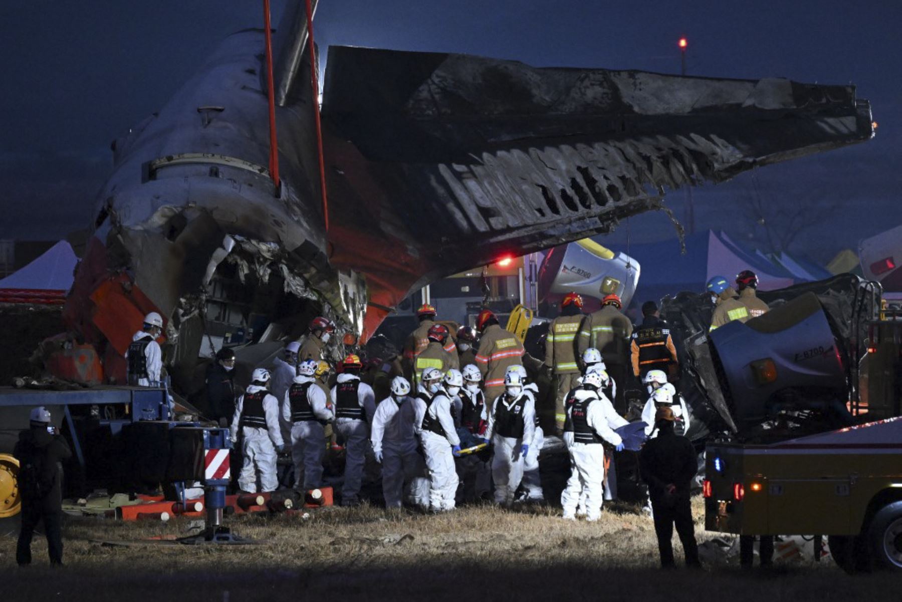 Los bomberos y el personal de rescate llevan el cuerpo de una víctima cerca de la escena en la que un avión Boeing de la serie 737-800 de Jeju Air se estrelló y estalló en llamas en el Aeropuerto Internacional de Muan en la provincia del Sur de Jeolla, a unos 288 kilómetros al suroeste de Seúl el 29 de diciembre de 2024. Un avión de Jeju Air que transportaba a 181 personas de Tailandia a Corea del Sur se estrelló al llegar, estrellando contra una barrera y estallando en llamas, dejando a todos menos a dos t