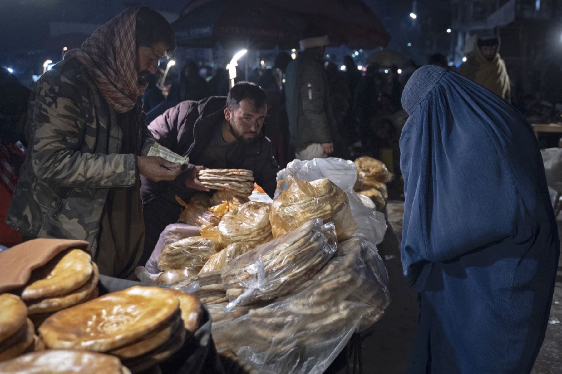 Esta fotografía muestra a una mujer afgana vestida de burka (R) comprando panes planos tradicionales conocidos localmente como Naan, en un mercado de carretera en Kabul. Para muchos en Afganistán, uno de los países más pobres del mundo, donde 12,4 millones de personas viven en inseguridad alimentaria aguda, según el Programa Mundial de Alimentos, el pan constituye la mayor parte de las comidas. El pan afgano es uno de los pocos alimentos que todo el mundo puede permitirse, con precios tan bajos como 10 afganos (0,14) centavos. Foto: AFP