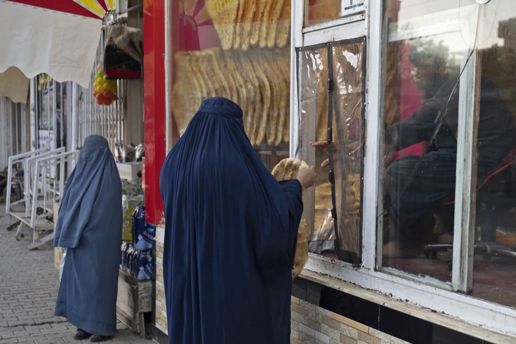 Esta fotografía muestra a una mujer afgana vestida con burka (C) comprando panes planos tradicionales conocidos localmente como Naan, de una panadería al borde de la carretera en Kabul. Para muchos en Afganistán, uno de los países más pobres del mundo, donde 12,4 millones de personas viven en inseguridad alimentaria aguda, según el Programa Mundial de Alimentos, el pan constituye la mayor parte de las comidas. El pan afgano es uno de los pocos alimentos que todo el mundo puede permitirse, con precios tan bajos como 10 afganos (0,14) centavos. Foto: AFP