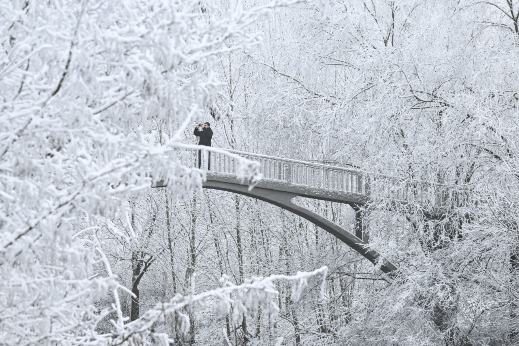 Un hombre toma una foto mientras cruza un puente después de la nevada en un parque en el terraplén del río Main en Frankfurt am Main, al oeste de Alemania, el 29 de diciembre de 2024. (Foto de Kirill KUDRYAVTSEV / AFP)