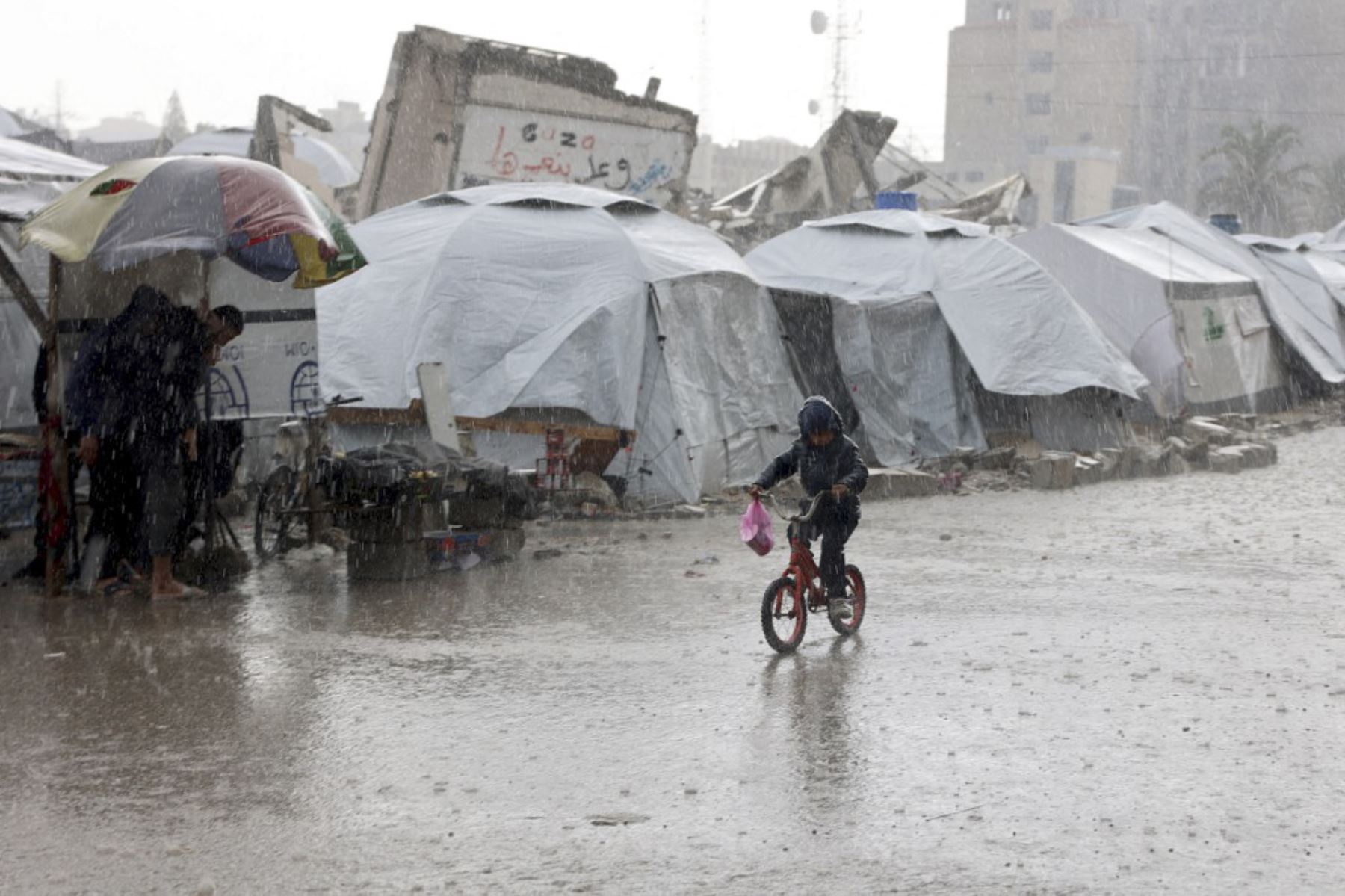 Un niño palestino pasa en bicicleta por tiendas de campaña empapadas durante una tormenta de lluvia en un campamento improvisado en la ciudad de Gaza el 31 de diciembre de 2024, en medio de la continua guerra entre Israel y el grupo militante Hamas. (Foto de Omar AL-QATTAA / AFP)