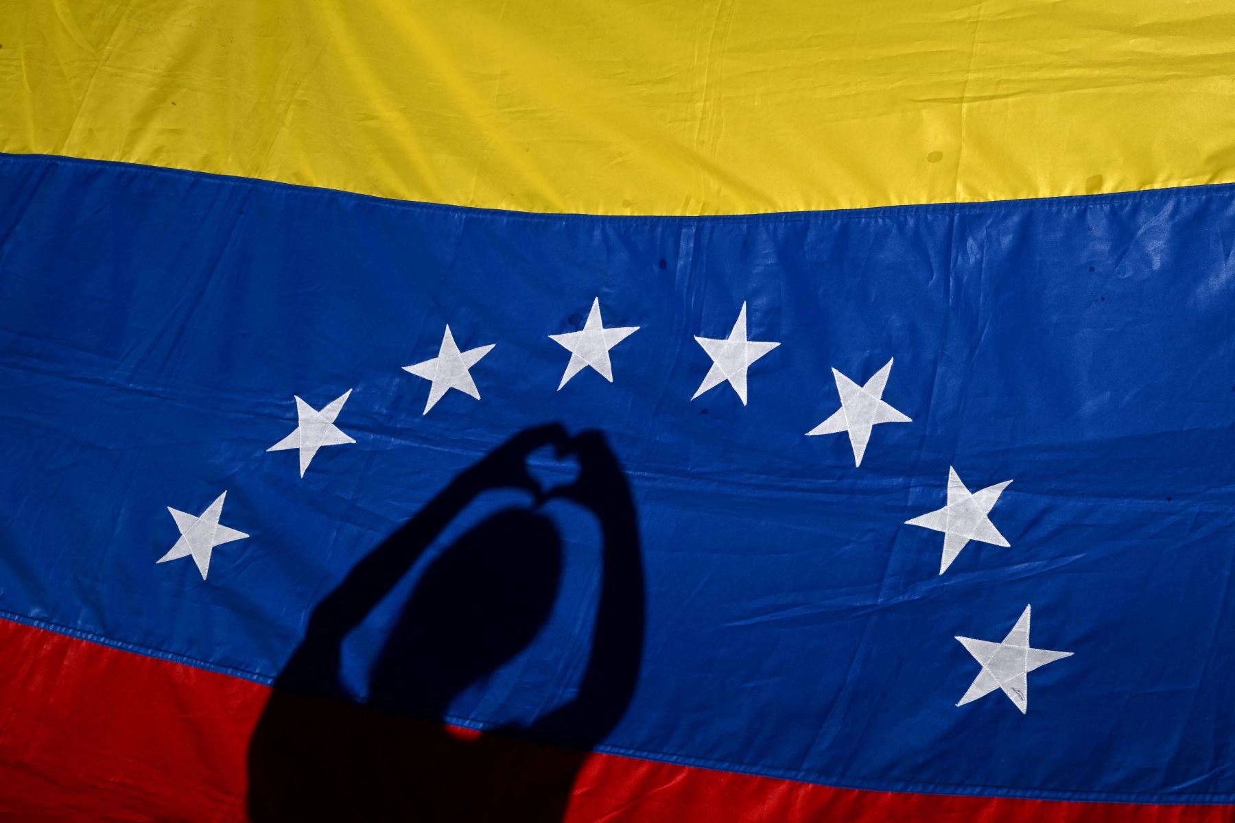 Las sombras de un residente venezolano se reflejan en una bandera venezolana durante una protesta en vísperas de la toma de posesión del presidente de Venezuela, Nicolás Maduro, en Buenos Aires. Foto: AFP