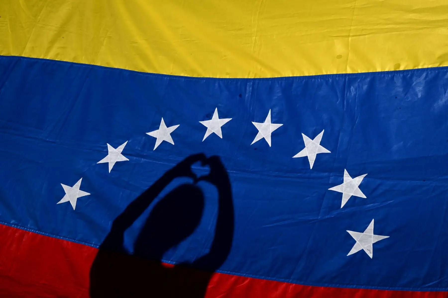 Las sombras de un residente venezolano se reflejan en una bandera venezolana durante una protesta en vísperas de la toma de posesión del presidente de Venezuela, Nicolás Maduro, en Buenos Aires. Foto: AFP