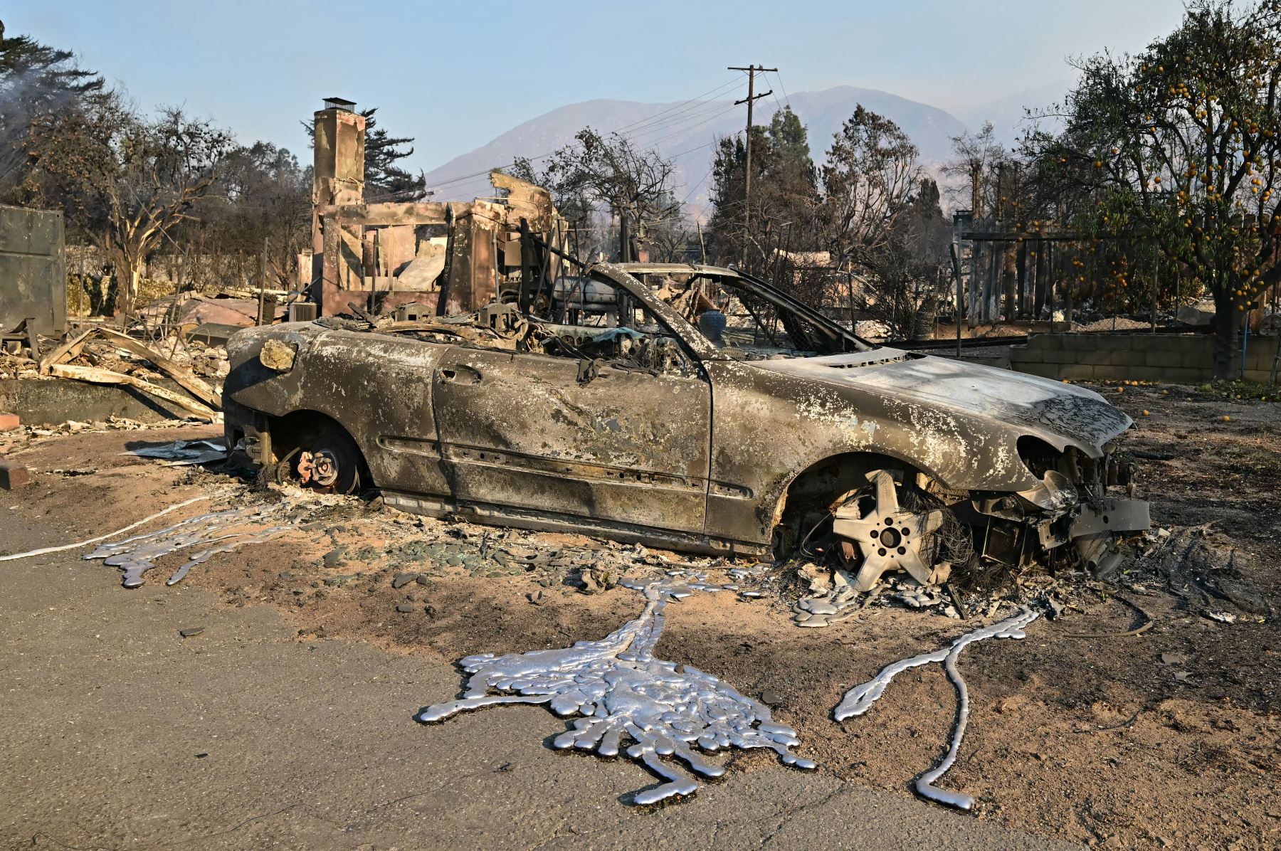 Un automóvil parcialmente derretido se encuentra cerca de casas quemadas destruidas por el incendio Eaton en Altadena, California. AFP