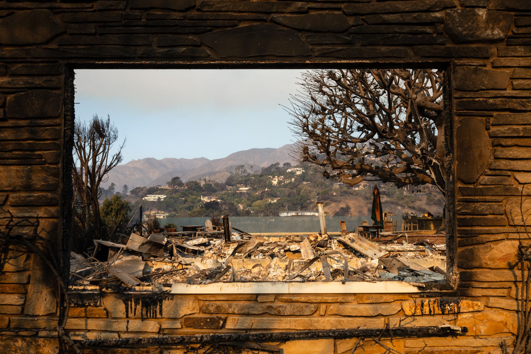 The rubble of a home destroyed in the Palisades Fire is seen through a window frame in the Pacific Palisades neighborhood of Los Angeles, California, AFP