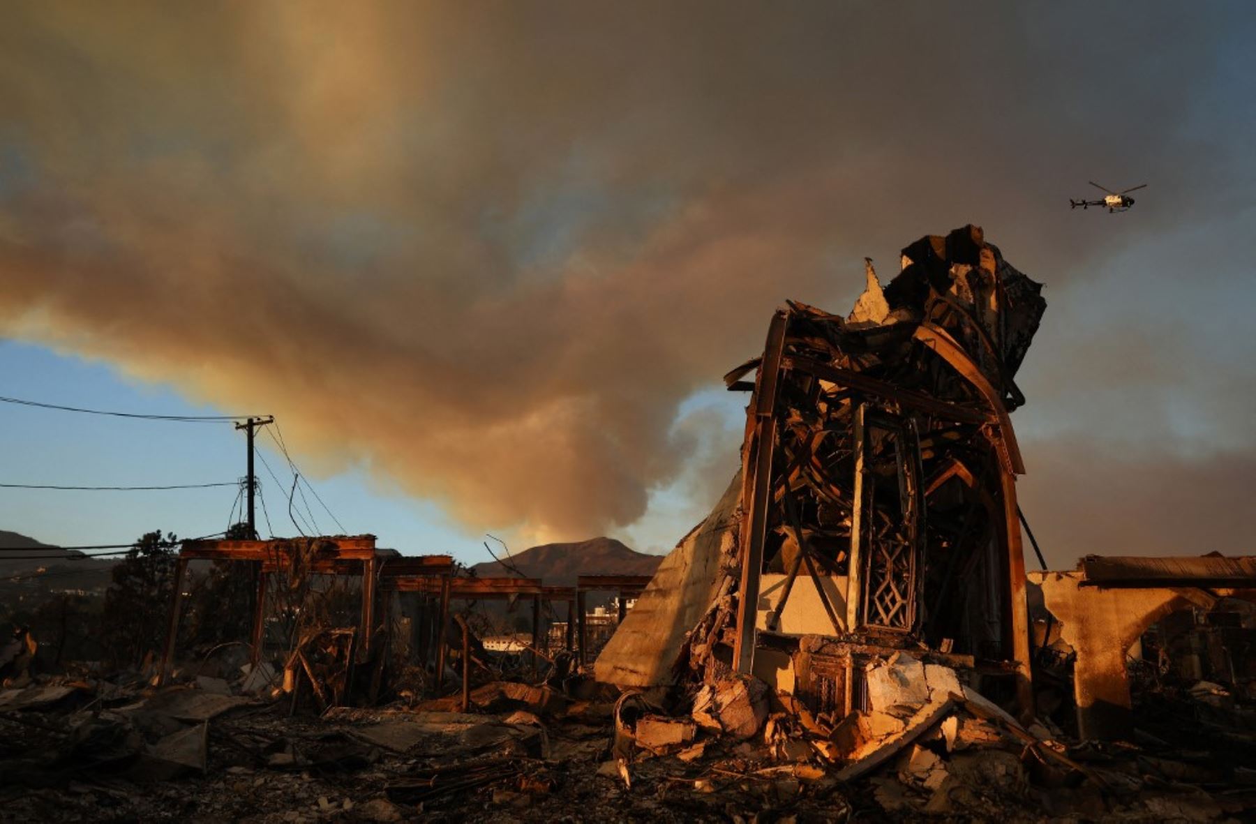 El incendio de Palisades continúa ardiendo sobre los restos de la Iglesia Metodista Unida Comunitaria, con un helicóptero de la policía volando mientras los incendios forestales causan daños y pérdidas en el condado de Los Ángeles. Foto: AFP