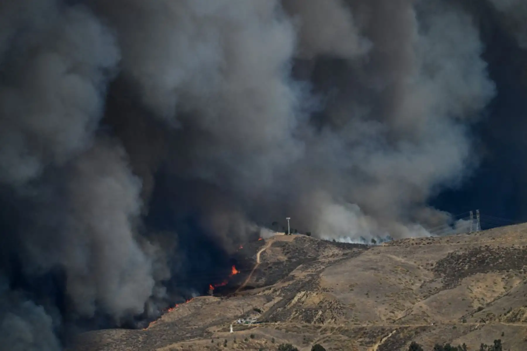 Las llamas suben la colina mientras la columna de humo del nuevo incendio Hughes llena el cielo en Castaic, un barrio del noroeste de Los Ángeles, California. Foto: AFP