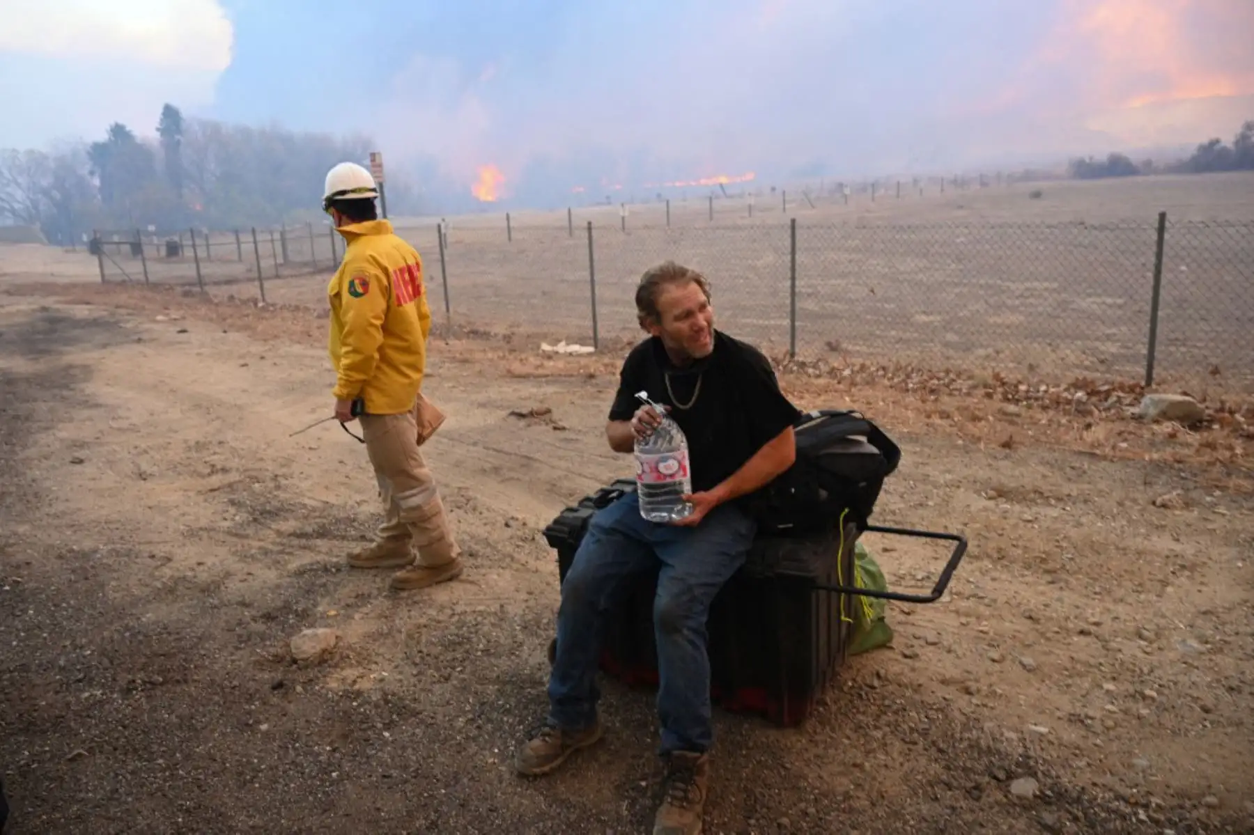 Un hombre que salió de la zona del incendio recibe agua mientras la columna de humo del incendio de Hughes llena el cielo en Castaic, una parte noroeste de Los Ángeles, California. Foto: AFP