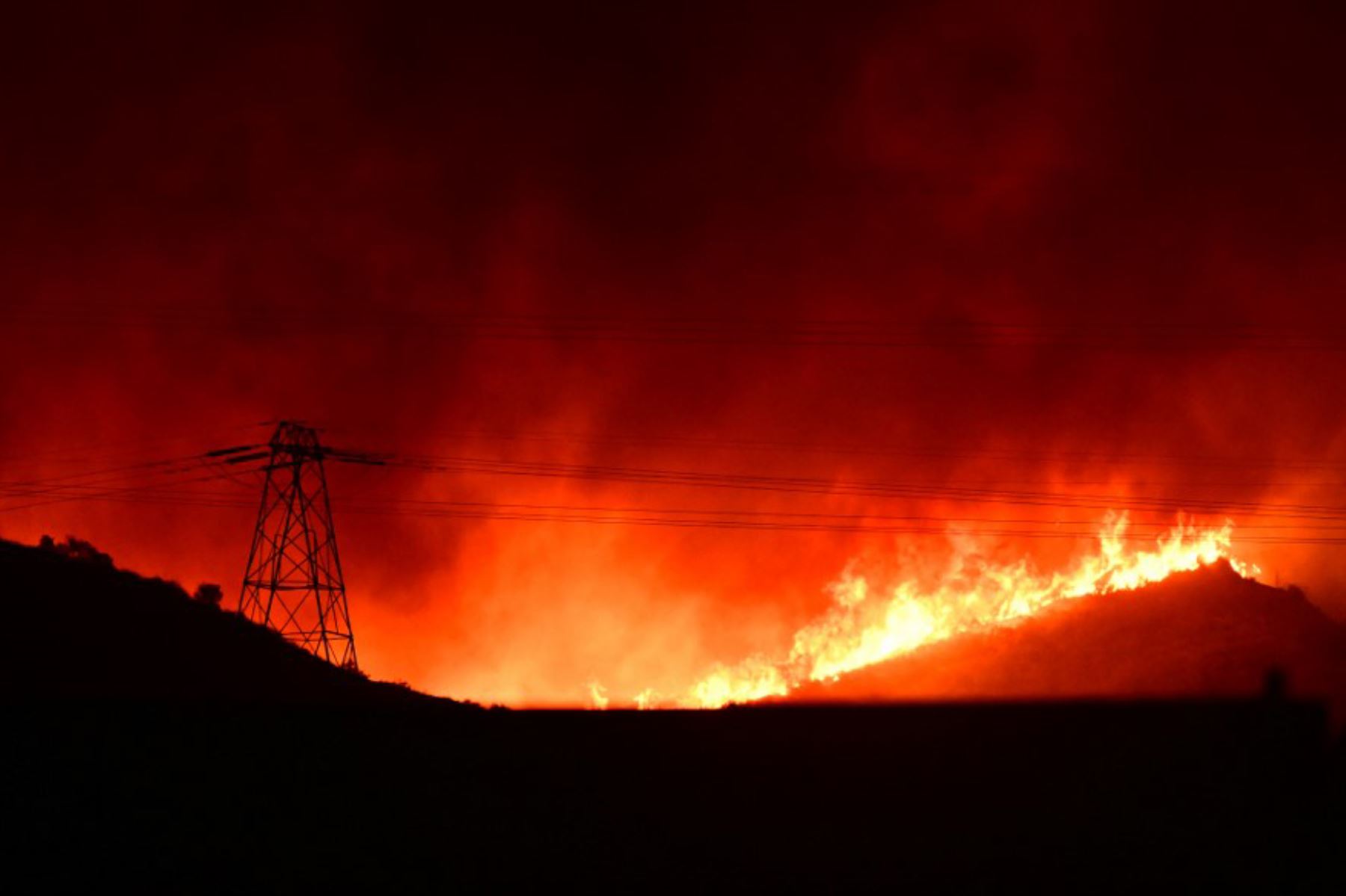 Llamas rojas brillantes y humo se elevan desde el incendio Hughes detrás de las líneas de transmisión eléctrica en Castaic, en el noroeste del condado de Los Ángeles, California. Foto: AFP