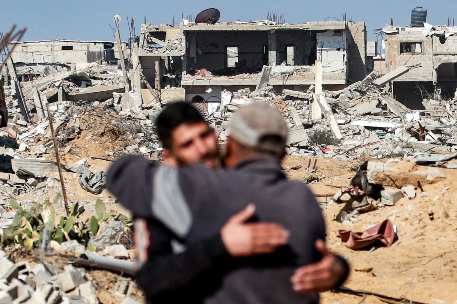 Dos hombres se abrazan cerca de edificios derrumbados en al-Shoka, al este de Rafah en el sur de la Franja de Gaza el 21 de enero de 2025 después de un acuerdo de alto el fuego en la guerra entre Israel y Hamas en el territorio palestino. (Foto de Bashar TALEB / AFP)