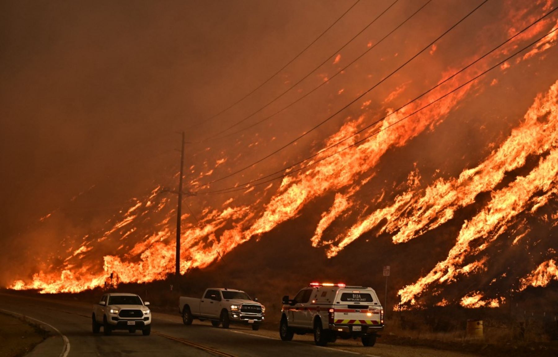 Los vehículos de emergencia están a un lado de la carretera mientras las llamas del Hughes Fire corren por la colina en Castaic, un barrio del noroeste de Los Ángeles, California, el 22 de enero de 2025. Un nuevo incendio forestal estalló al norte de Los Ángeles el 22 de enero, explotando en tamaño y provocando miles de órdenes de evacuación en una región que ya se tambaleaba por los efectos de enormes incendios. Foto. AFP