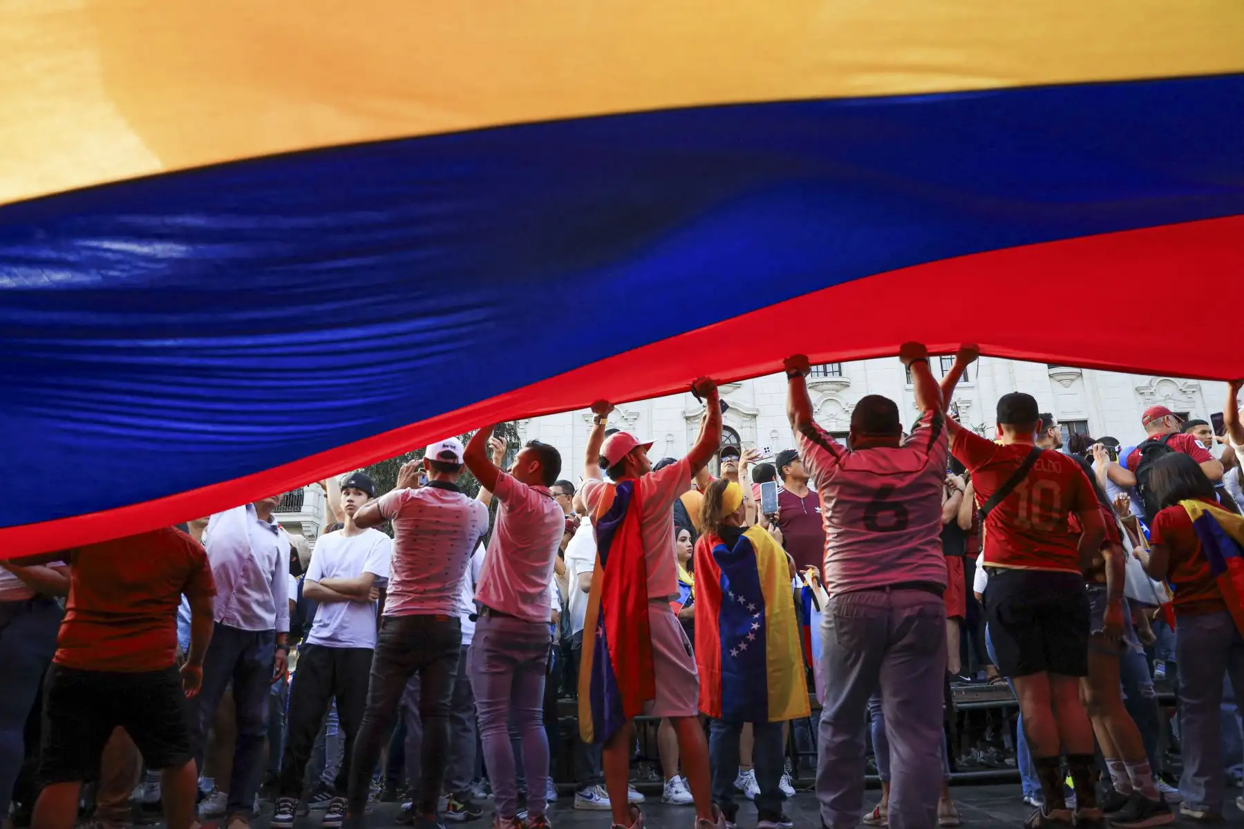Ciudadanos venezolanos ondean una bandera venezolana gigante mientras participan en una manifestación a favor de Edmundo González Urrutia en Lima. Foto: AFP