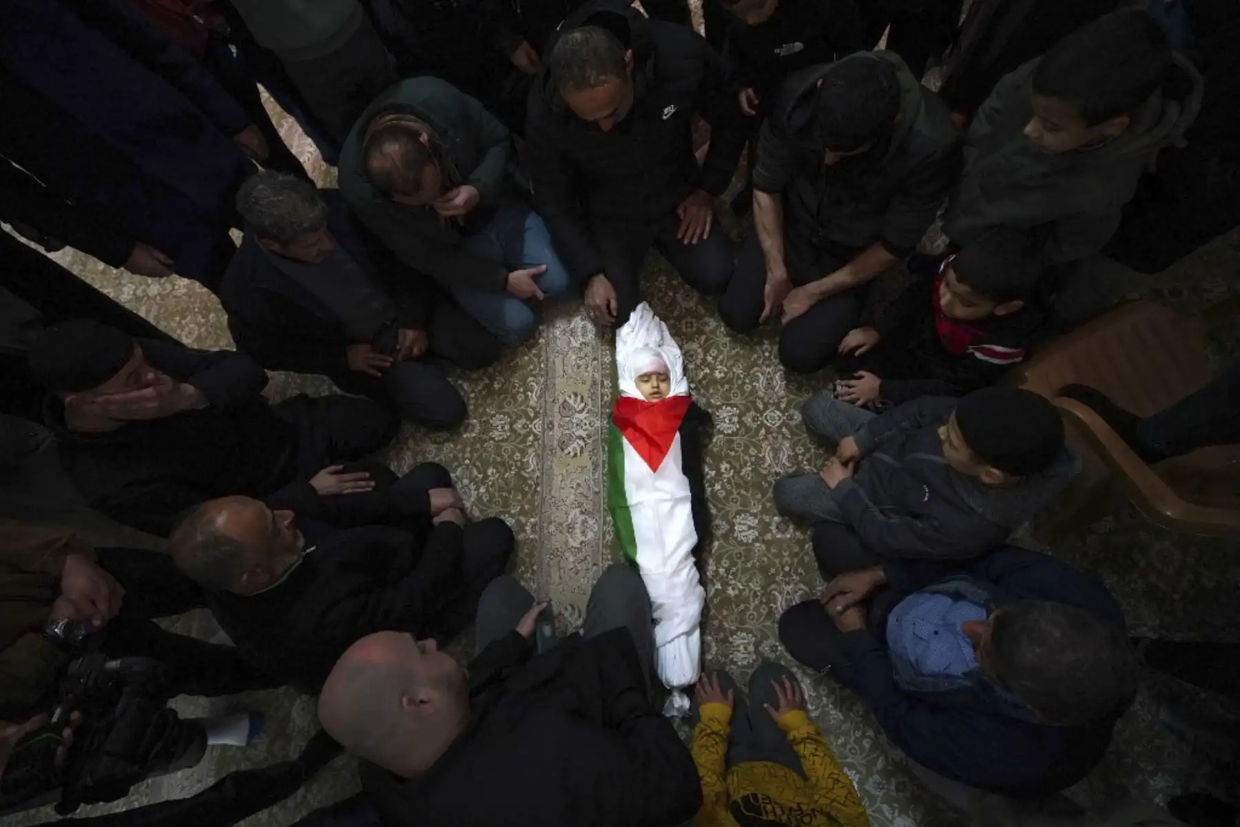 Los dolientes rodean el cuerpo cubierto con la bandera de Laila al-Khatib, de dos años, mientras yace en una mezquita, un día después de que sucumbiera a sus heridas después de que le dispararan durante una redada militar israelí en Jenin, en la Ribera Occidental ocupada, antes de su funeral el 26 de enero de 2025. (Foto de AFP)